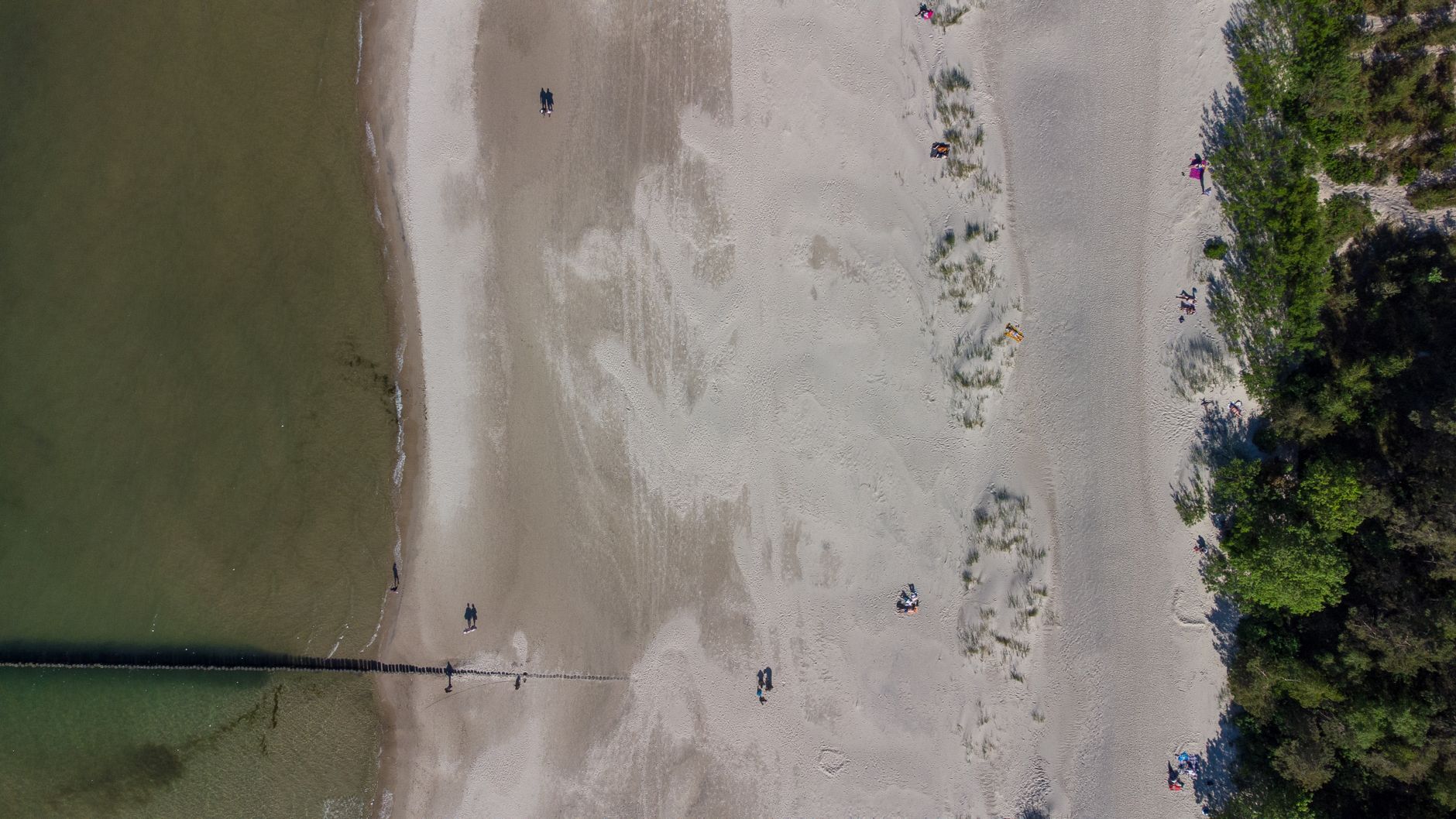 Bird's eye view of a sandy beach and shoreline in Ustka, Poland, with people walking.