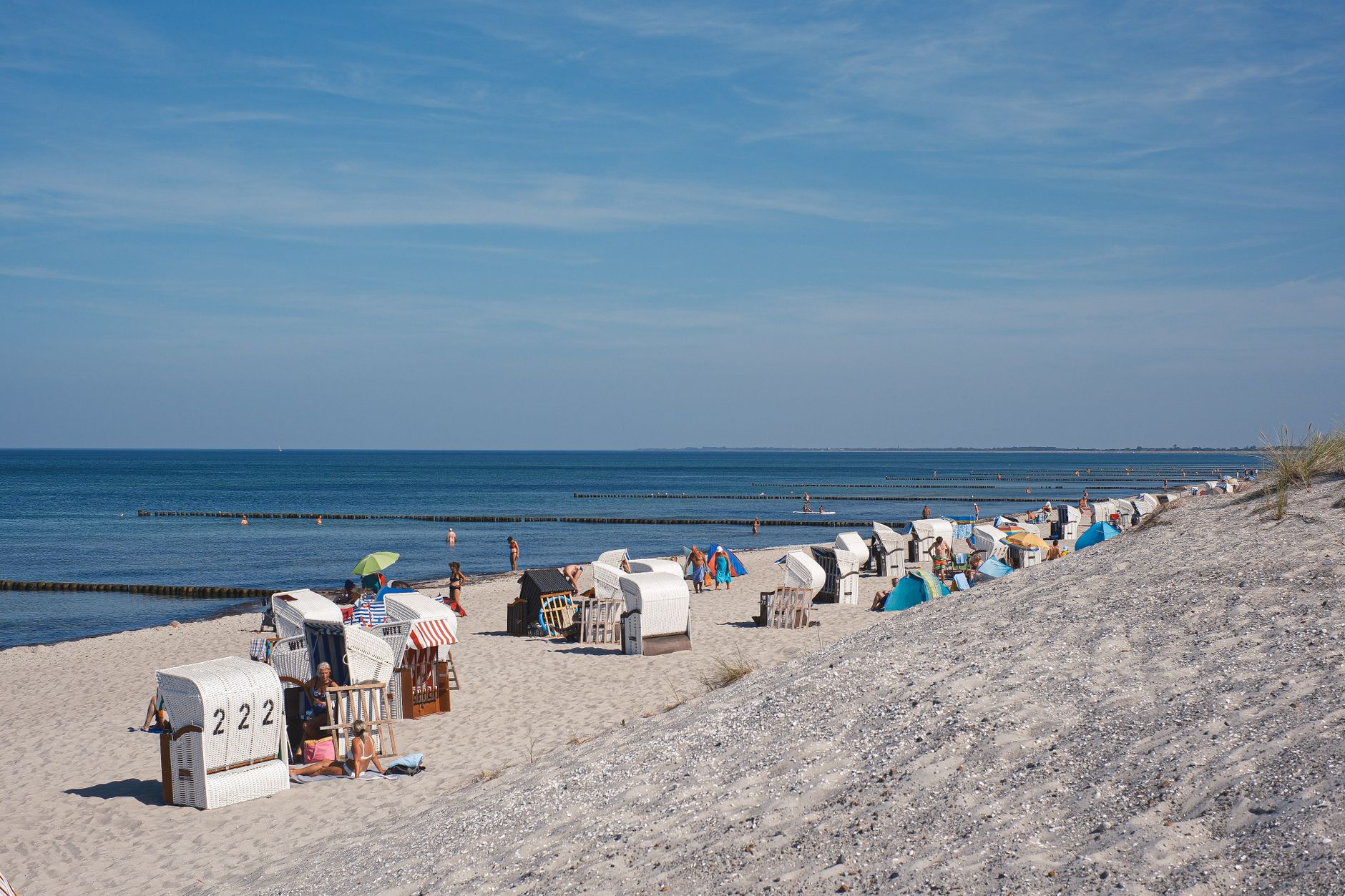 Sunny beach with straw huts, blue sea and visitors enjoying the sunny summer day. Ideal vacation spot.