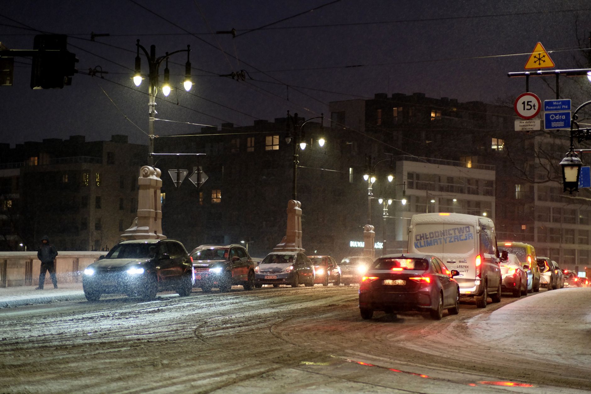 Vehicles navigate a snowy urban street under streetlights at night, showcasing winter traffic conditions.