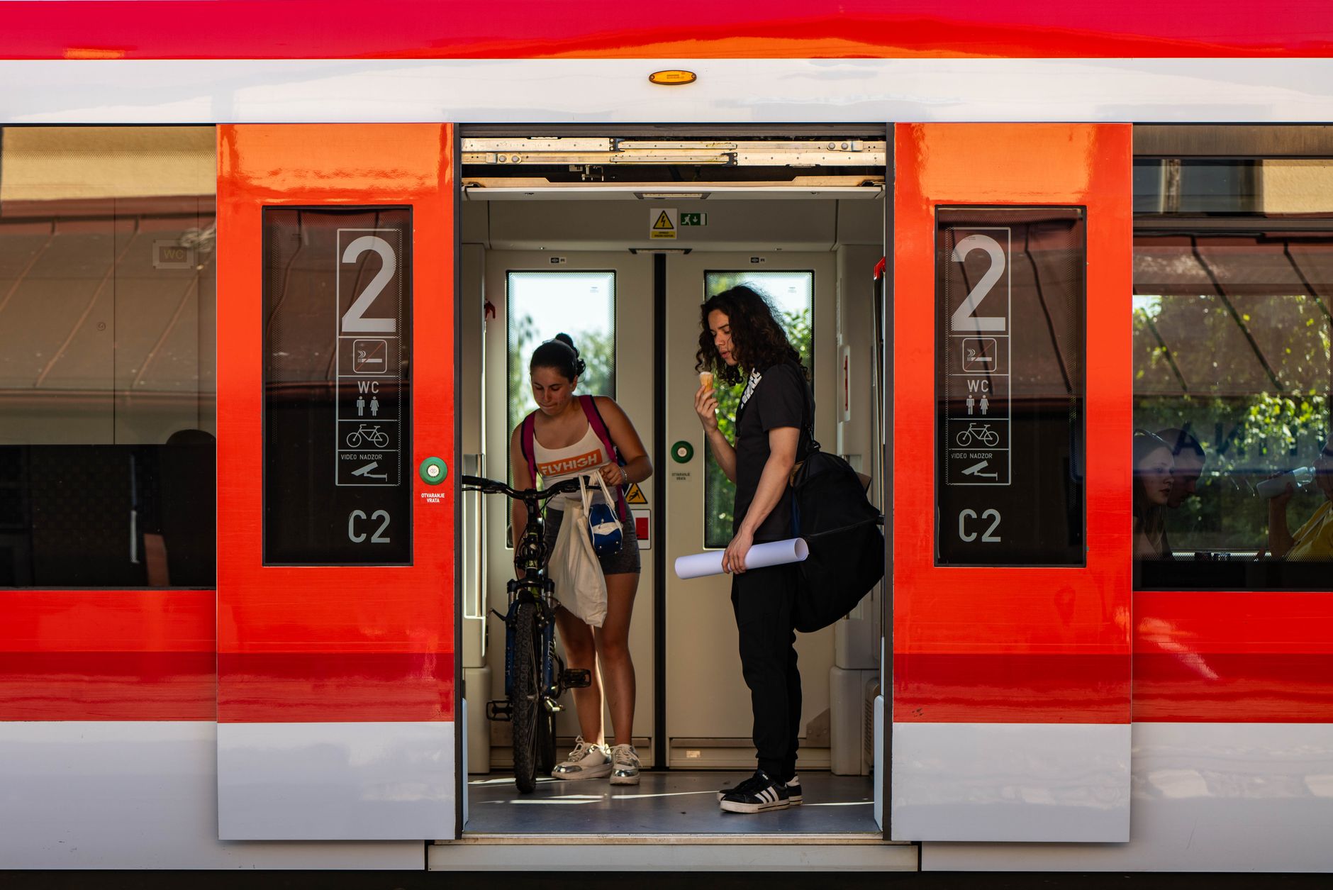 Two people with a bicycle stand at a train door, one eating ice cream.