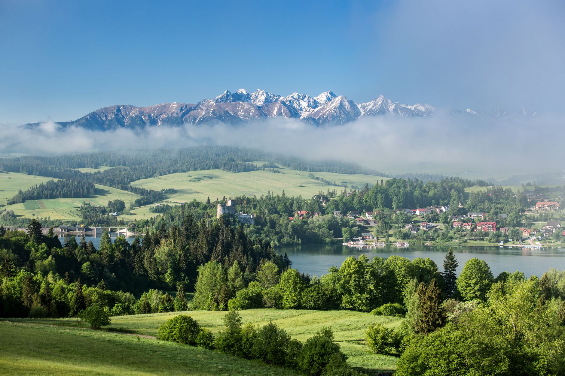 A breathtaking view of the Tatra Mountains enveloped in mist with a lush green landscape in the foreground.