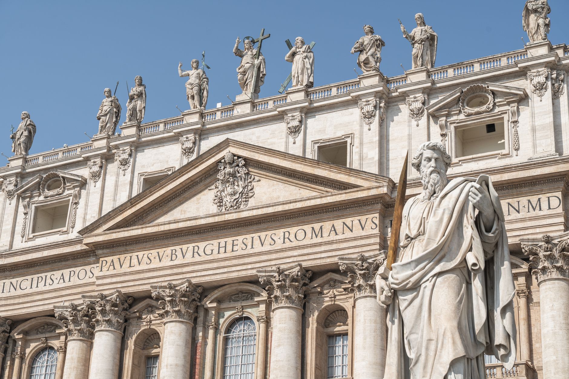 Statues of apostles adorn the facade of St. Peter's Basilica in Vatican City under a clear blue sky.