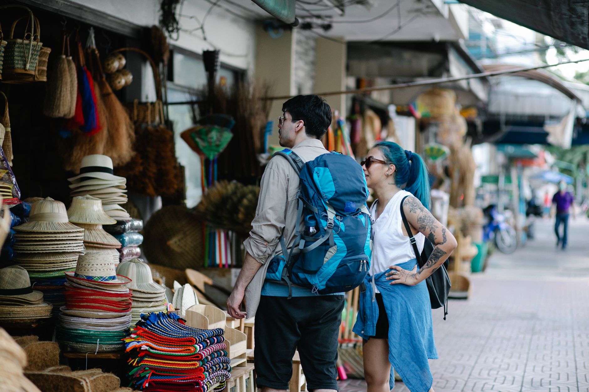 Tourists with backpacks admire diverse goods at a lively street market.