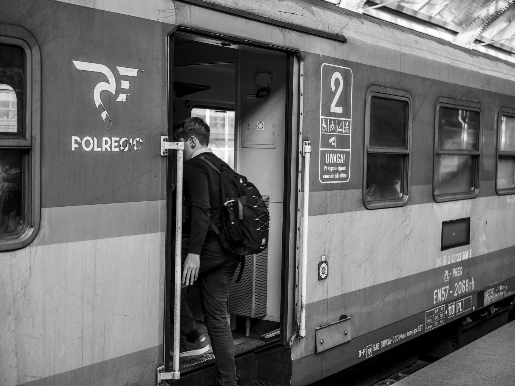 Black and white image of a person boarding a train at a city station.