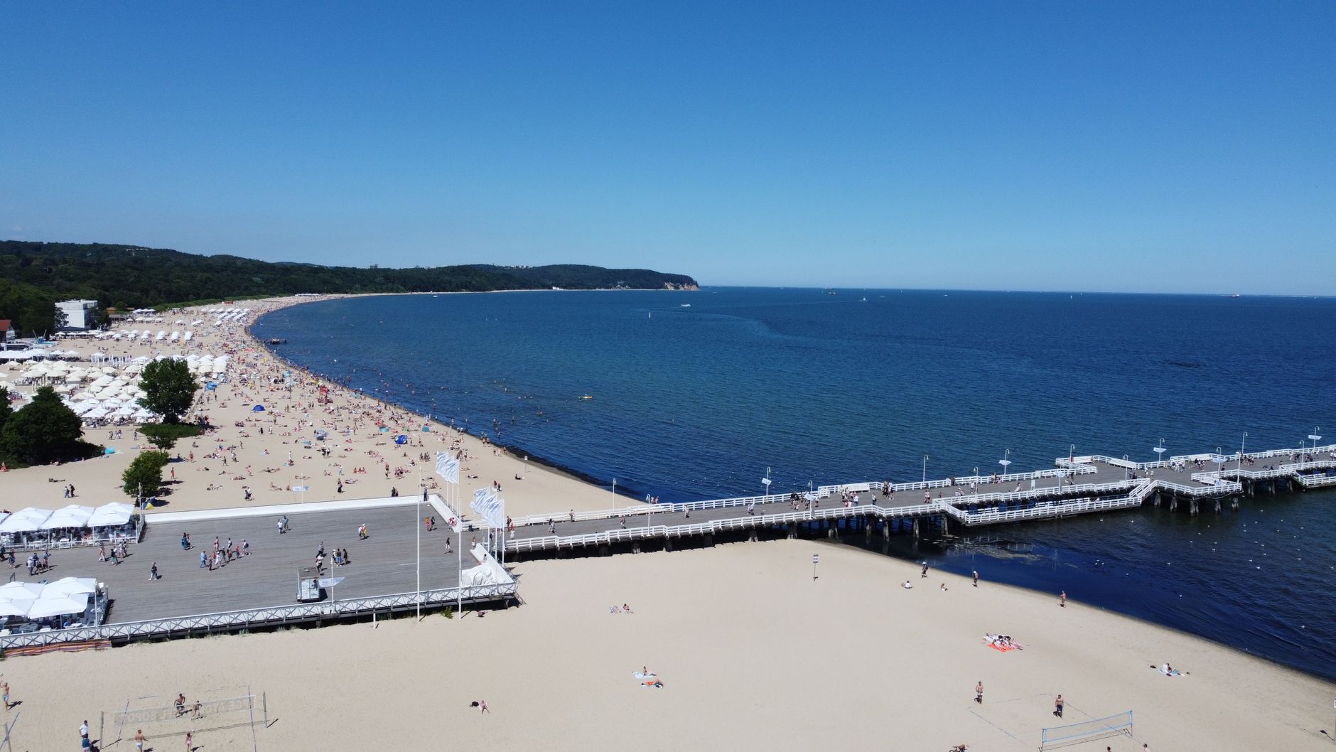 Explore the stunning aerial view of Sopot Pier and beach in Poland under clear blue skies.
