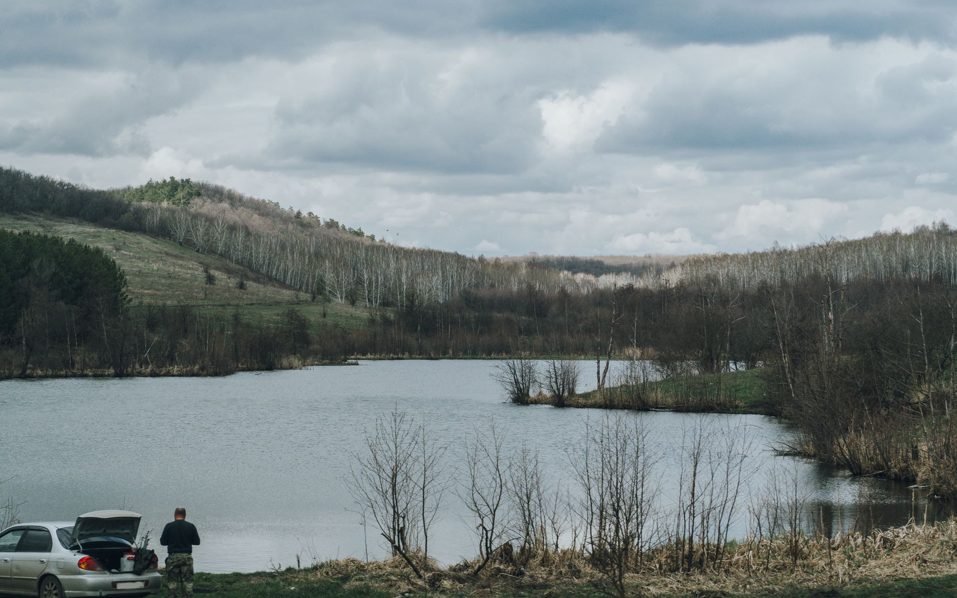 Beautiful lake scene with hills and a lone figure in Saratov, Russia under a cloudy sky.
