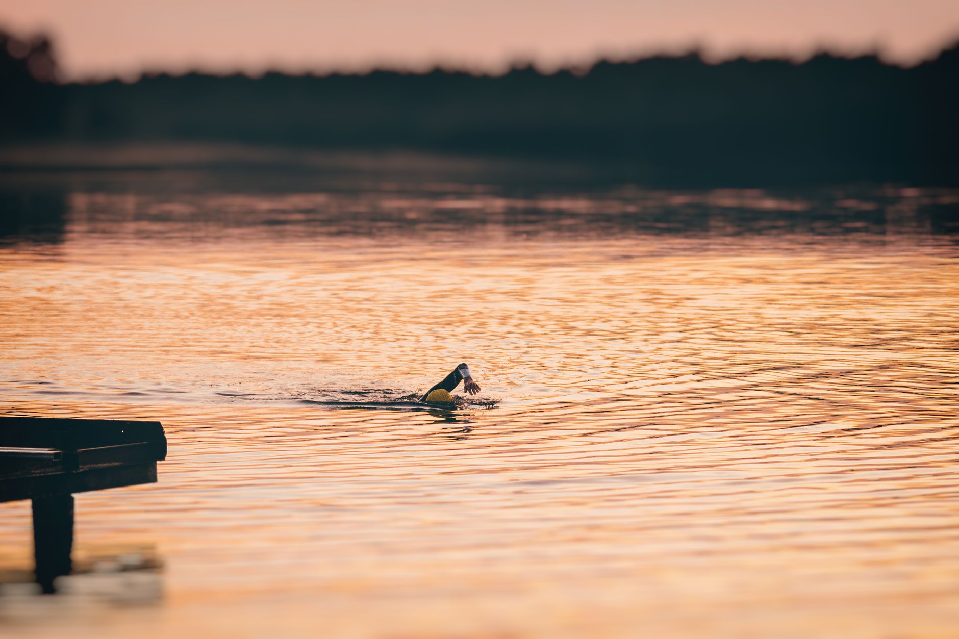 Person swimming in a tranquil lake during sunset, showcasing a serene and active lifestyle.