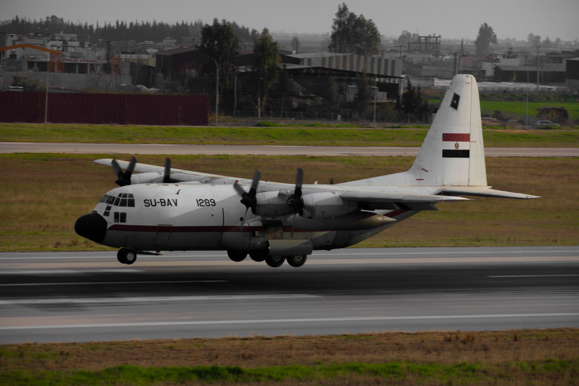 Military airplane with propellers landing on tarmac at an airport.