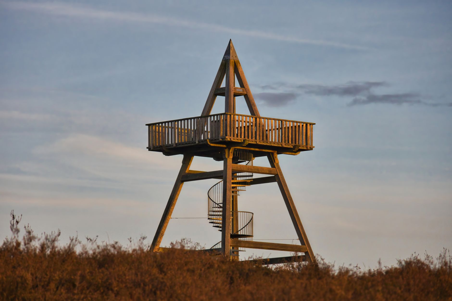 A wooden observation tower with a spiral staircase against a clear sky.