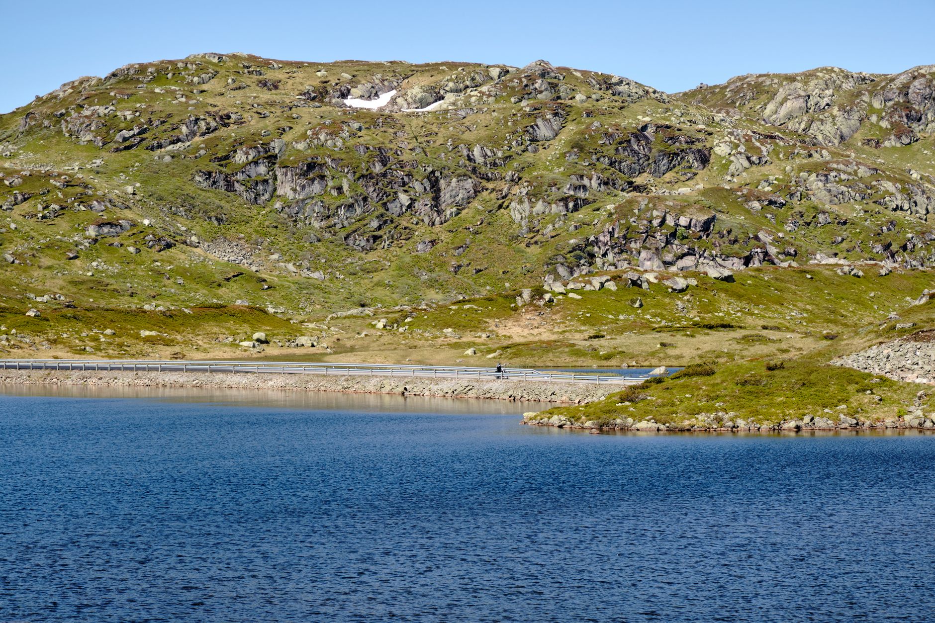 Serene mountain lake and rocky terrain under a clear sky.