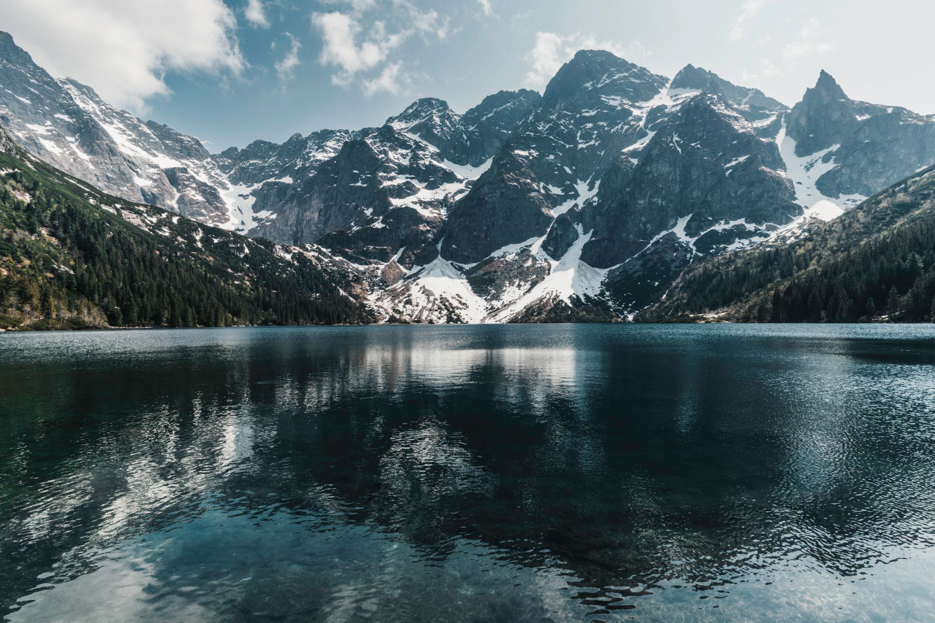 Stunning view of snow-capped mountains reflecting in a tranquil lake under a bright spring sky.