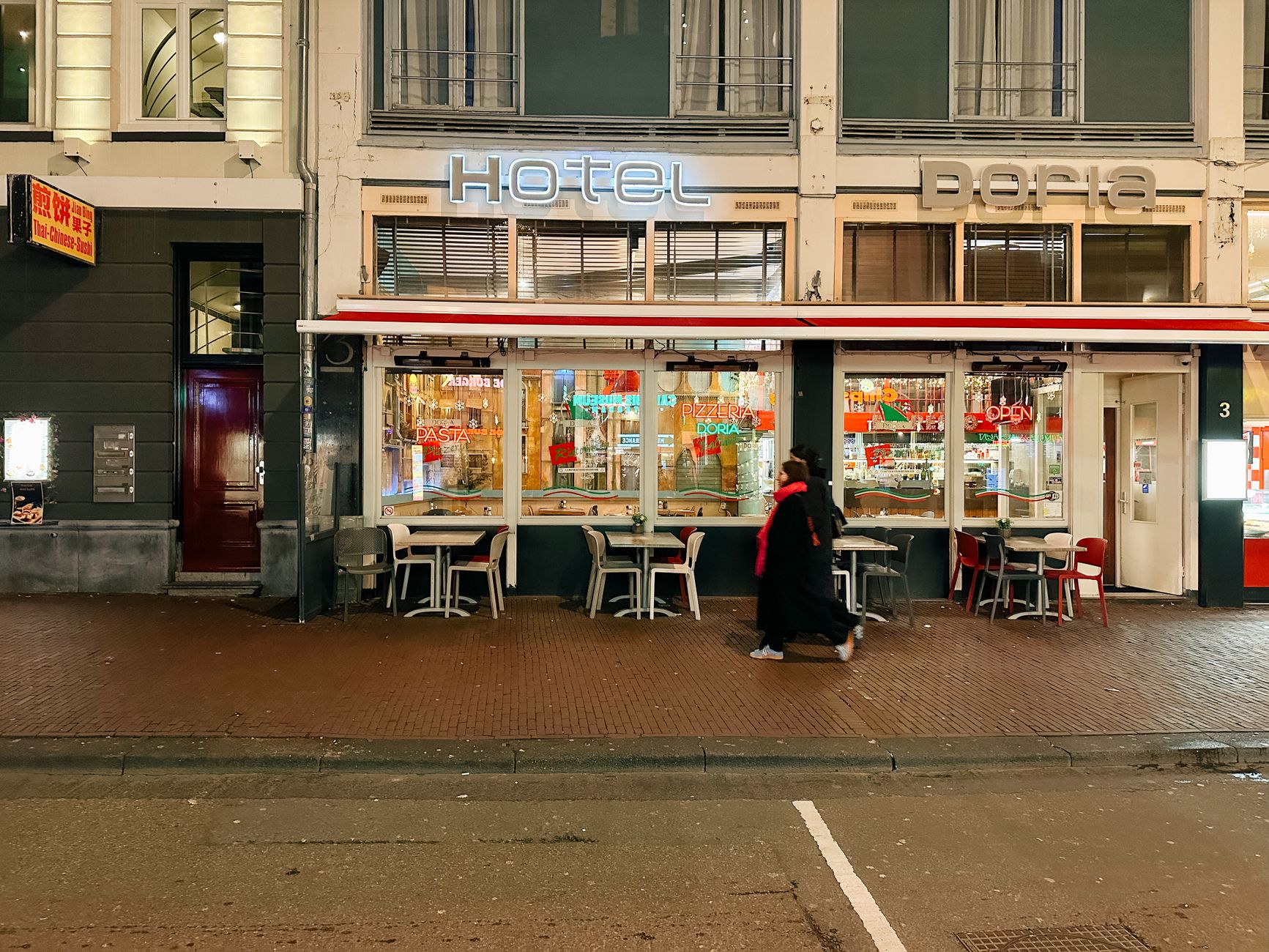 Street view of an illuminated bistro in Amsterdam's urban district, capturing a cozy evening atmosphere.