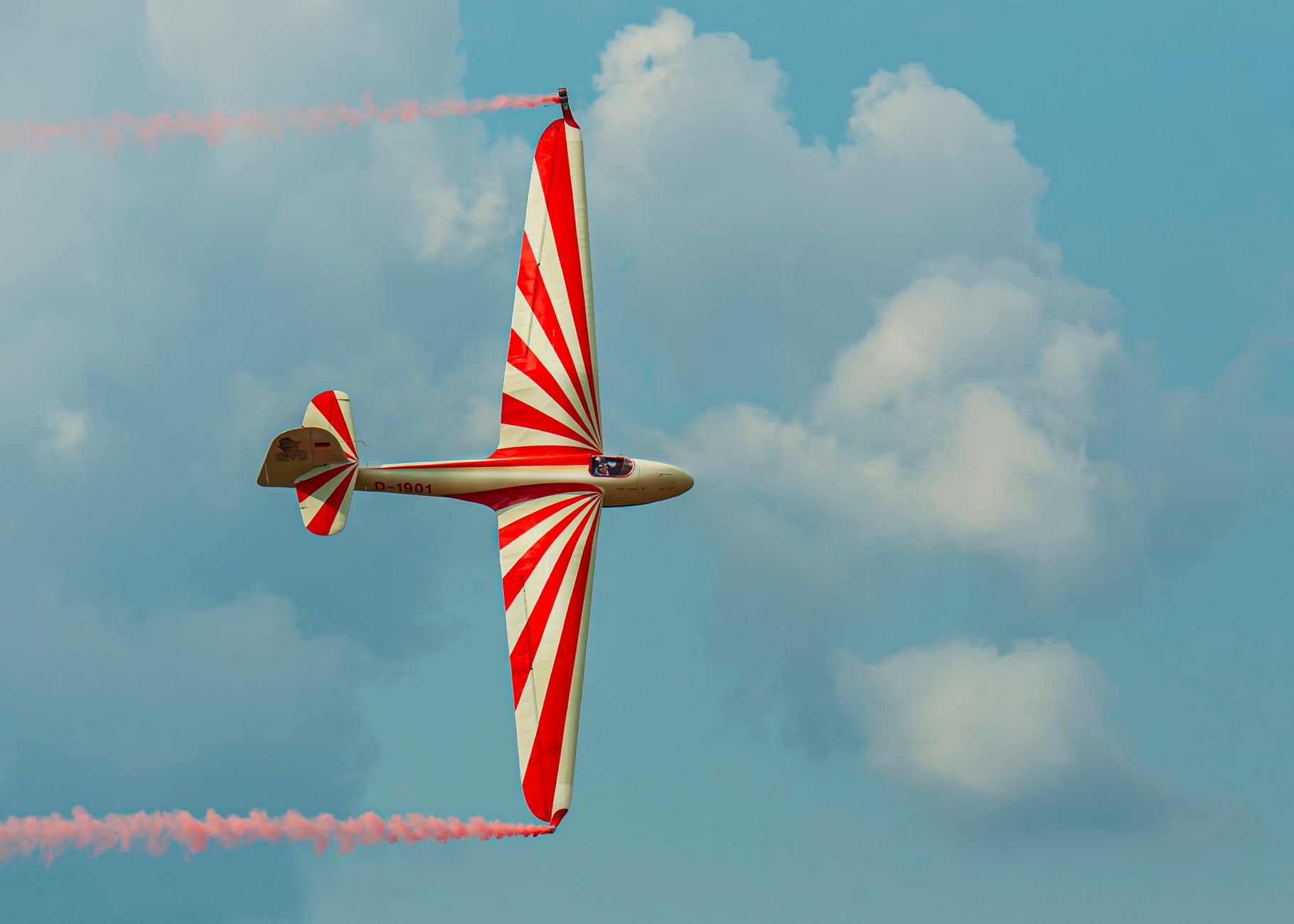 Aerobatic glider with red and white stripes soaring against a clear sky at an airshow.