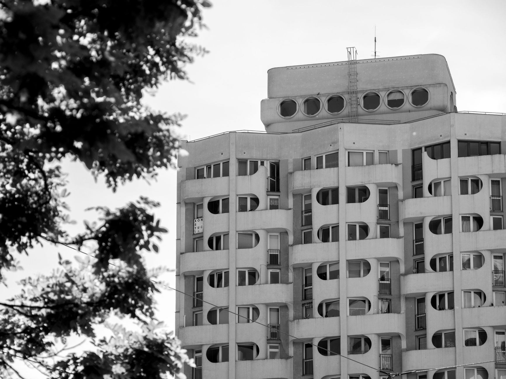 Black and white photo of a unique modernist building in Wrocław, Poland, with distinctive curves and circular windows.