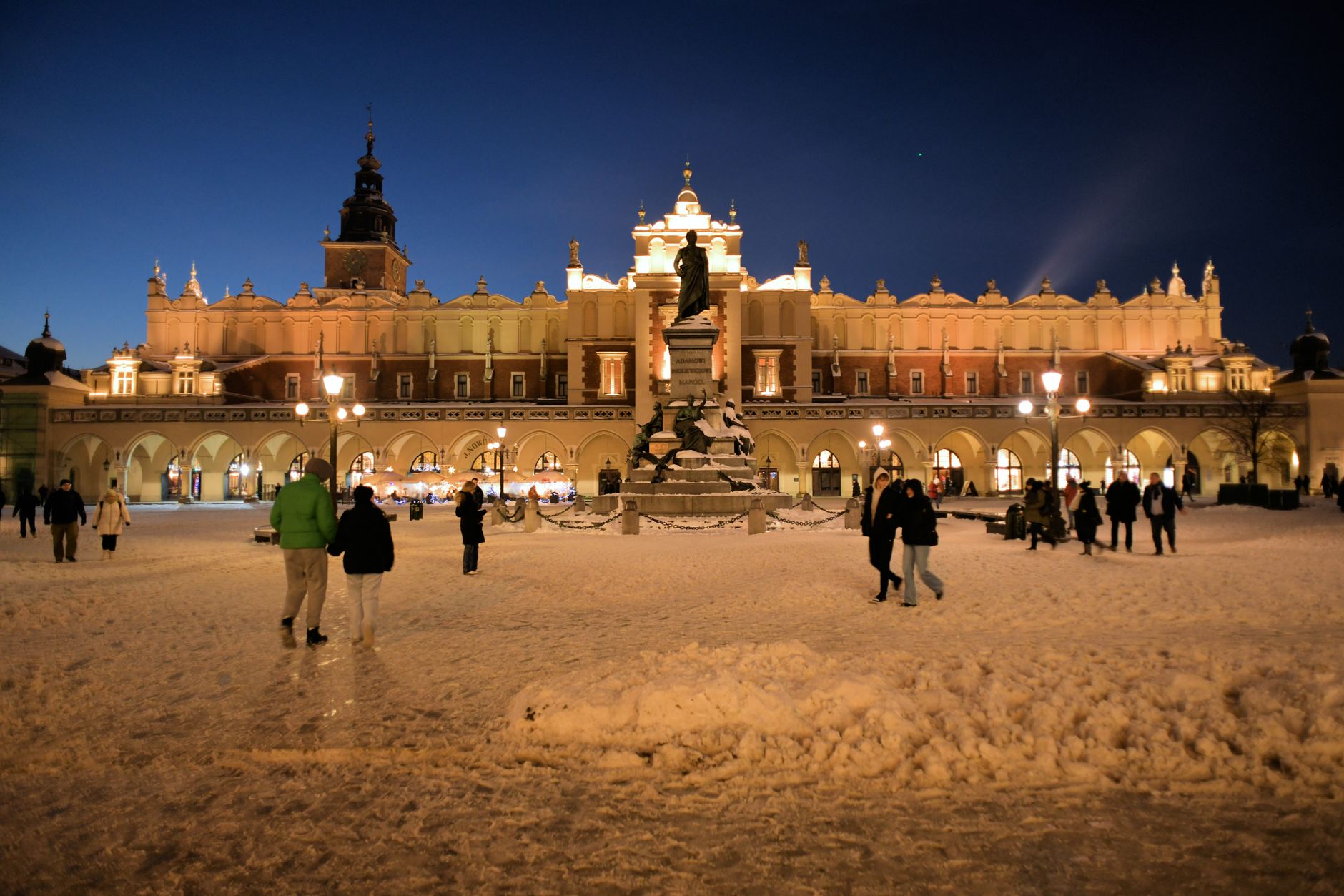 Illuminated Sukiennice and Mickiewicz Monument in Krakow at night covered in snow.