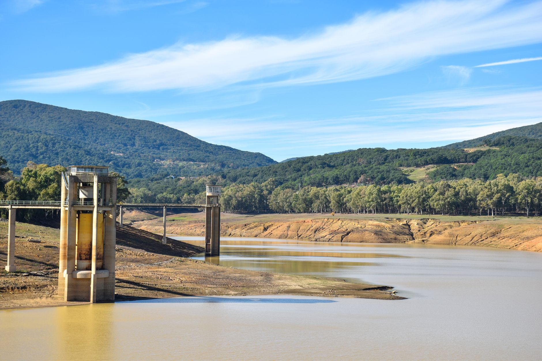 A striking view of a drought-affected reservoir surrounded by mountains and forest.