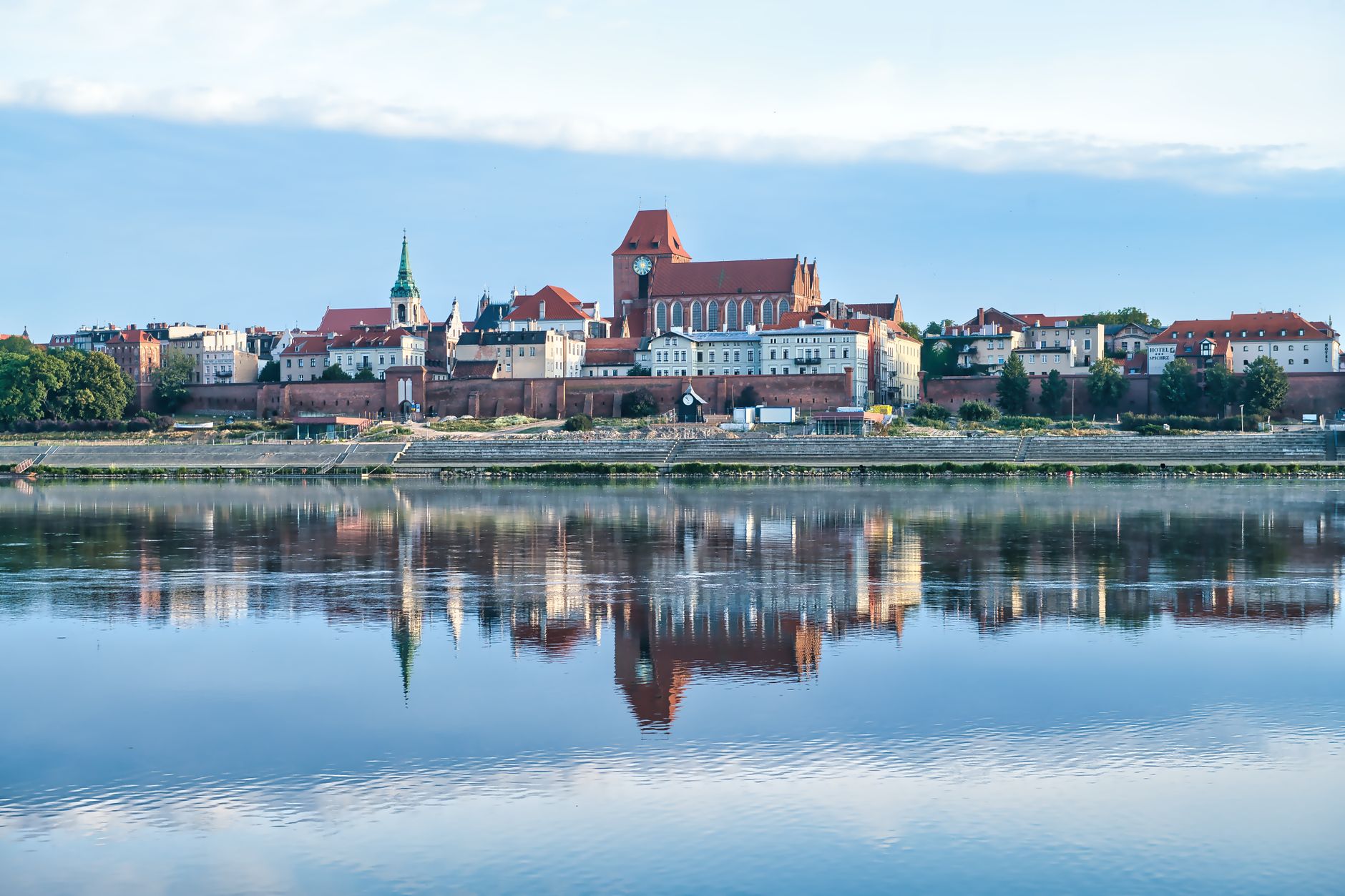 Panoramic view of Toruń's historical architecture reflecting across the Wisła River.