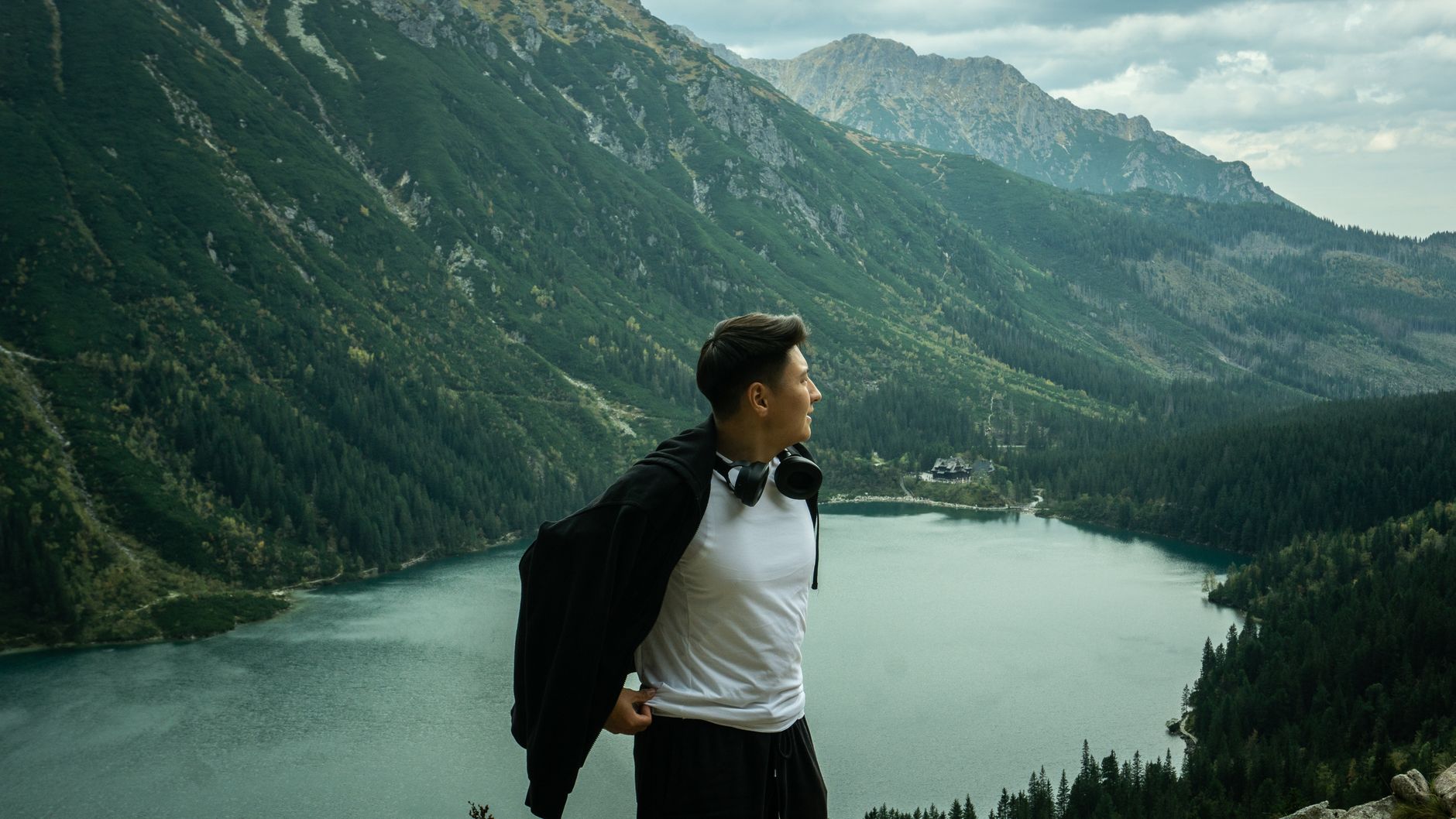 Young man relaxing by a serene mountain lake with lush greenery around.