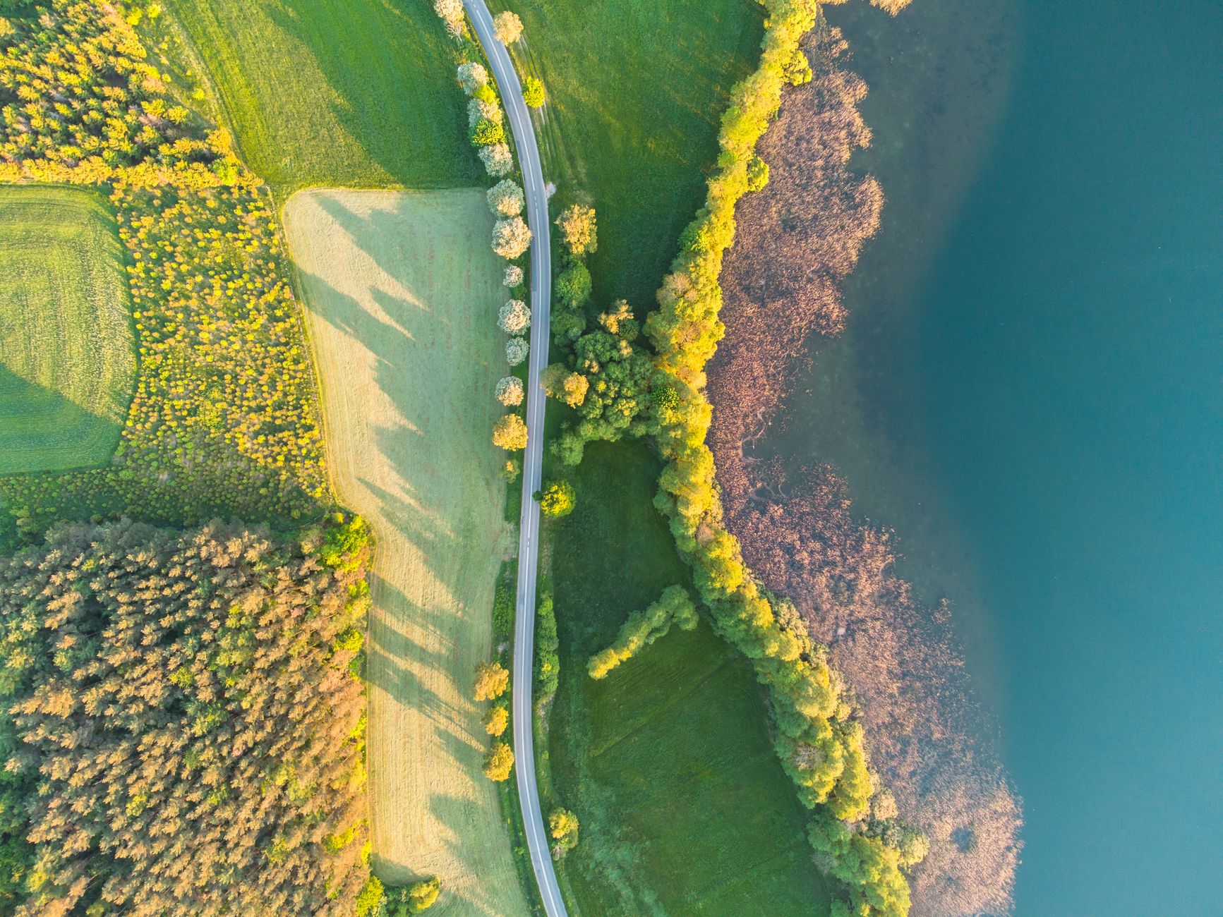 A captivating aerial shot of lush green fields, a winding road, and a glistening lake.