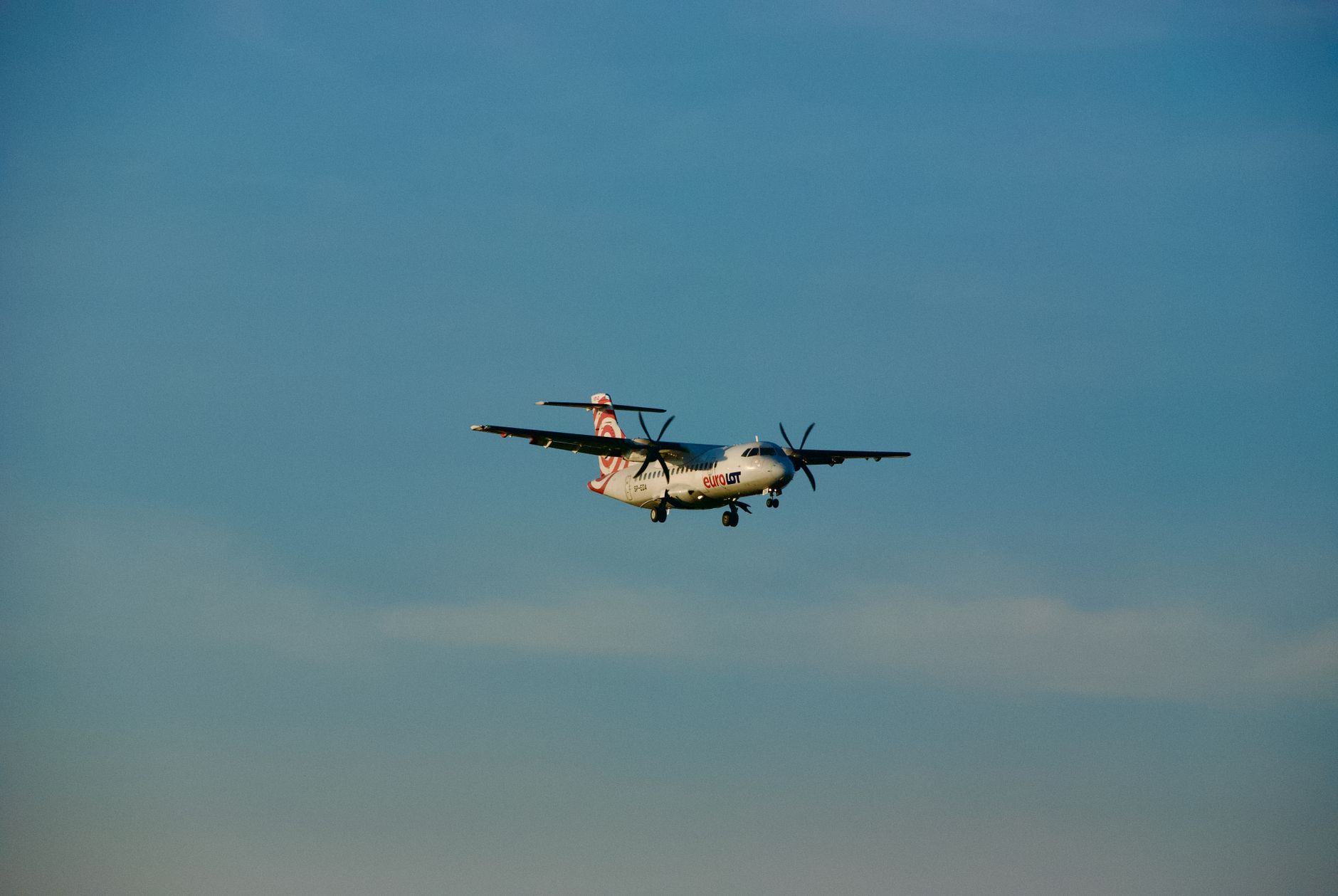 An ATR 72 airplane captured in flight approaching landing in a clear blue sky over Warsaw, Poland.