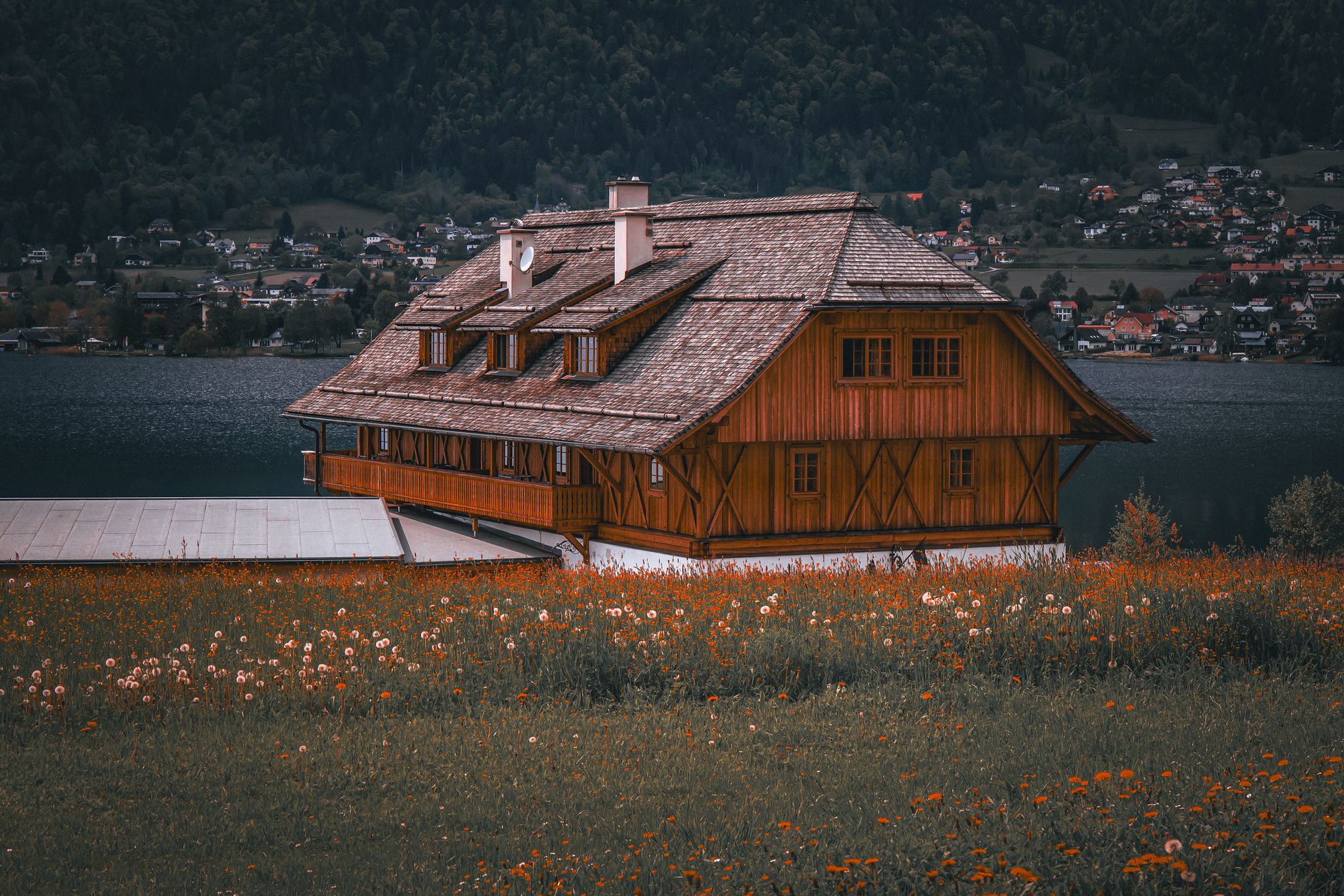 Charming rustic wooden house overlooking a serene lake with vibrant wildflowers in the foreground.