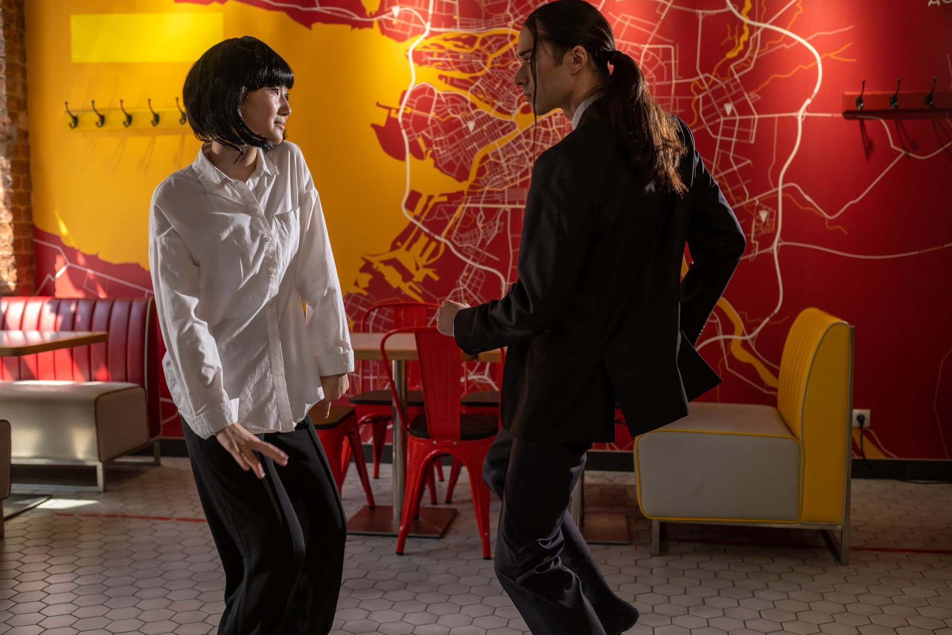A man and woman dancing joyfully inside a vibrant café with a map-themed wall.