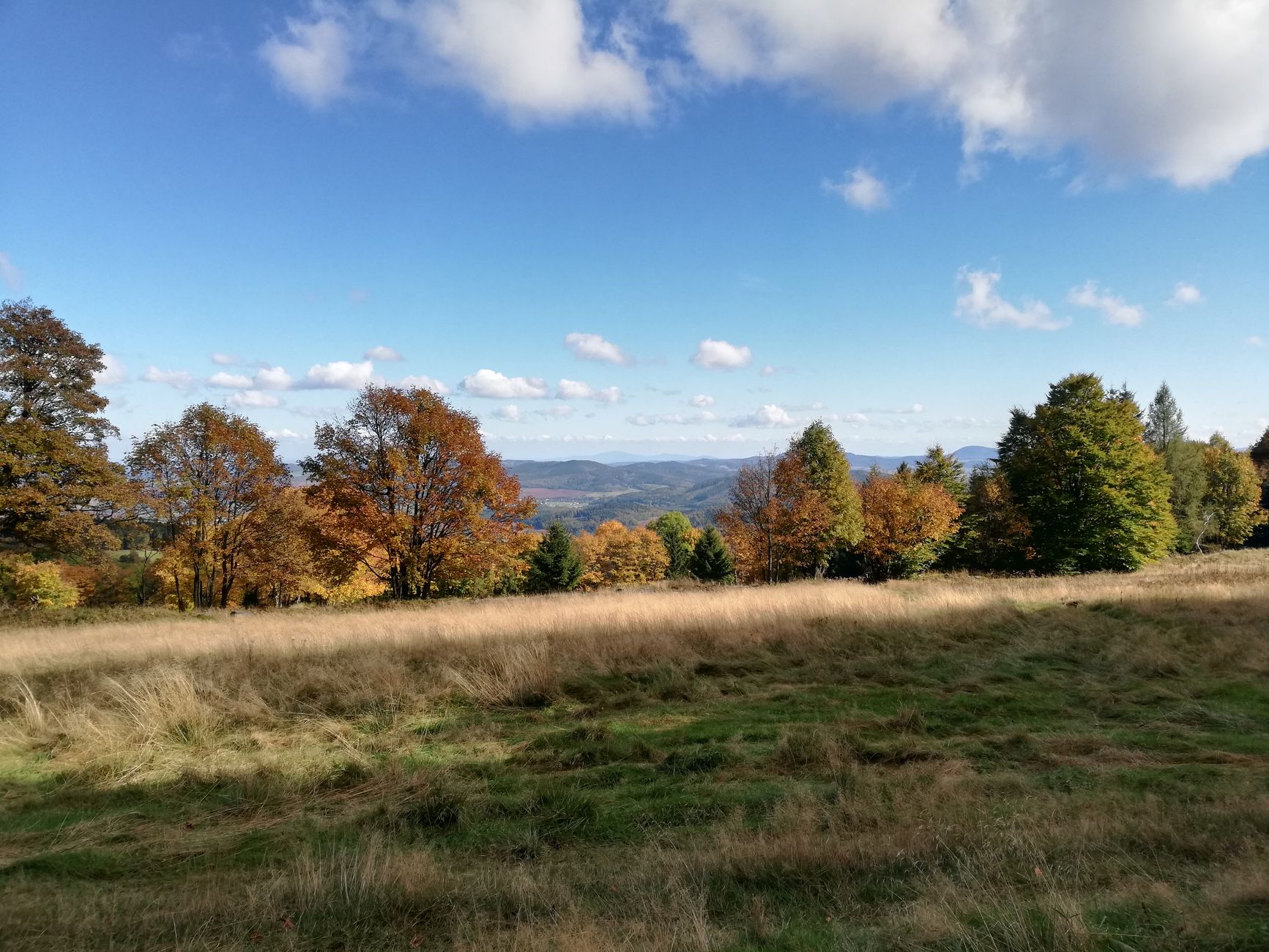 Scenic autumn view of Rudawy Janowickie with colorful foliage and rolling hills under a blue sky.