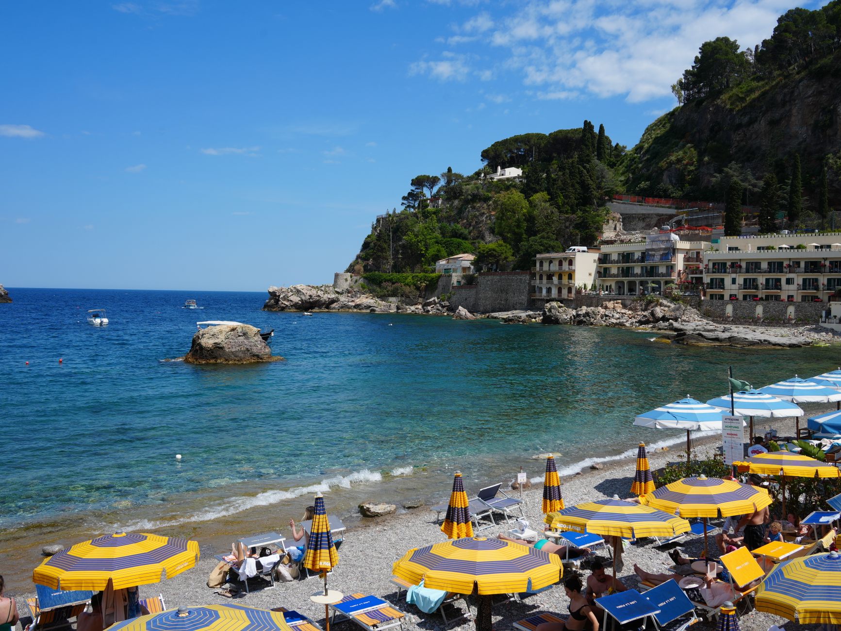 Sunny beach day in Taormina, Sicily, with colorful umbrellas and stunning coastal views.