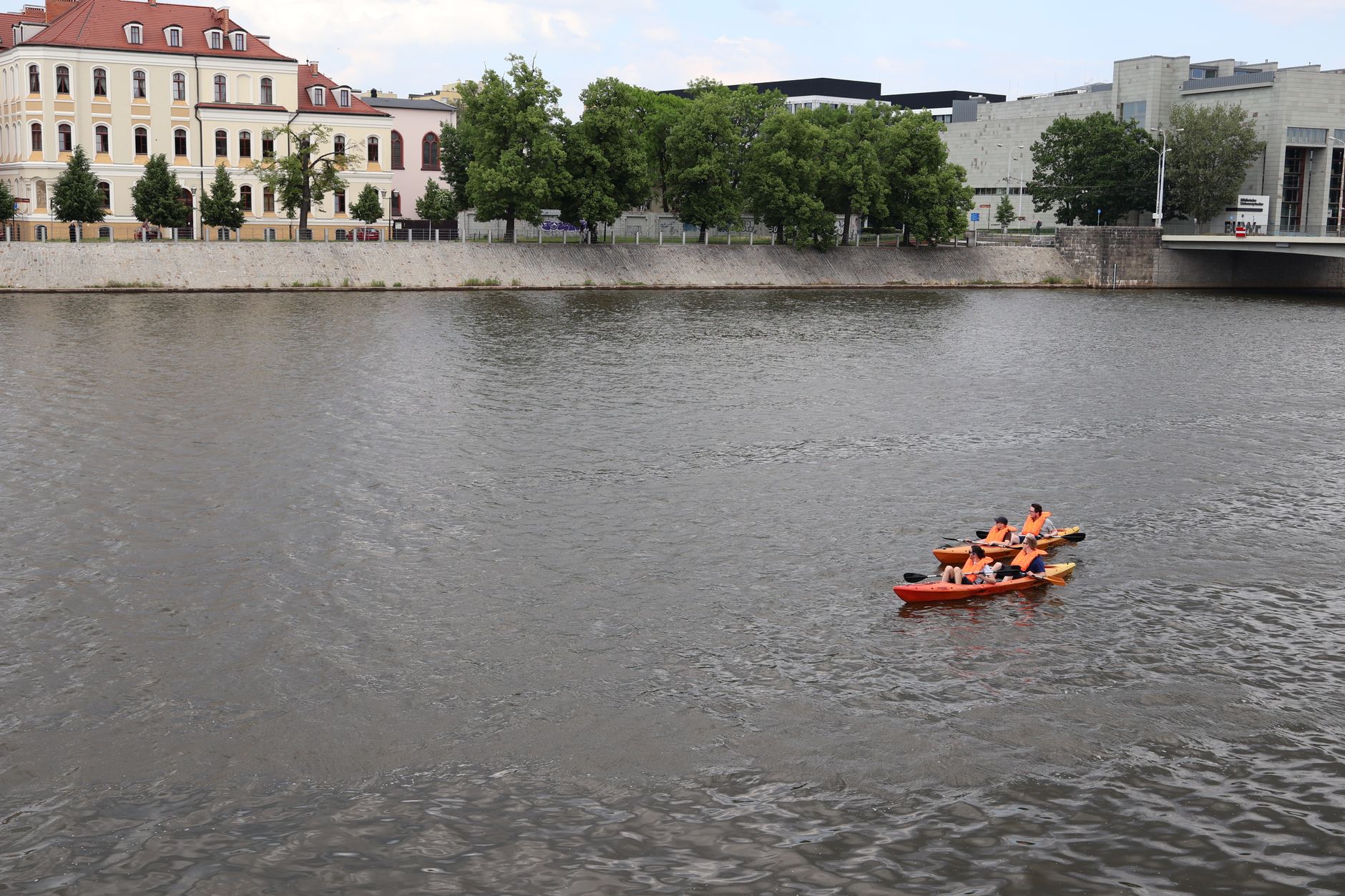 Colorful kayakers paddle on the Oder River against a backdrop of historic Wrocław architecture.