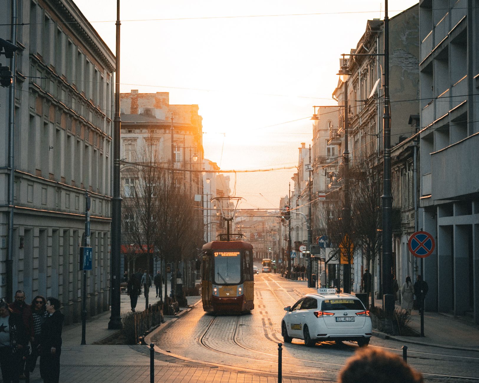 A picturesque sunset over a busy street in Łódź, featuring a tram and urban architecture.