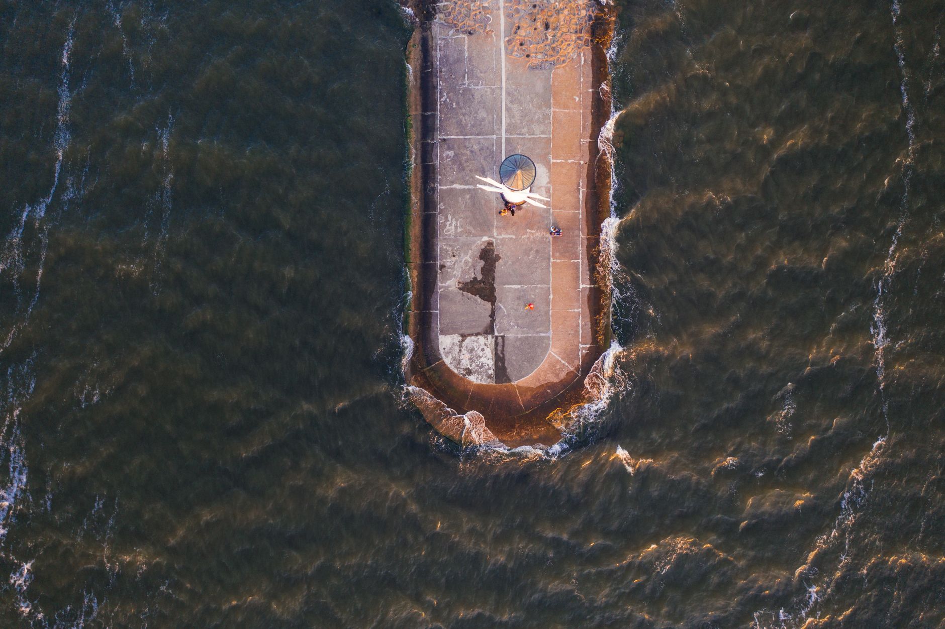 Drone shot of Swinoujscie lighthouse pier surrounded by ocean waves in Poland.