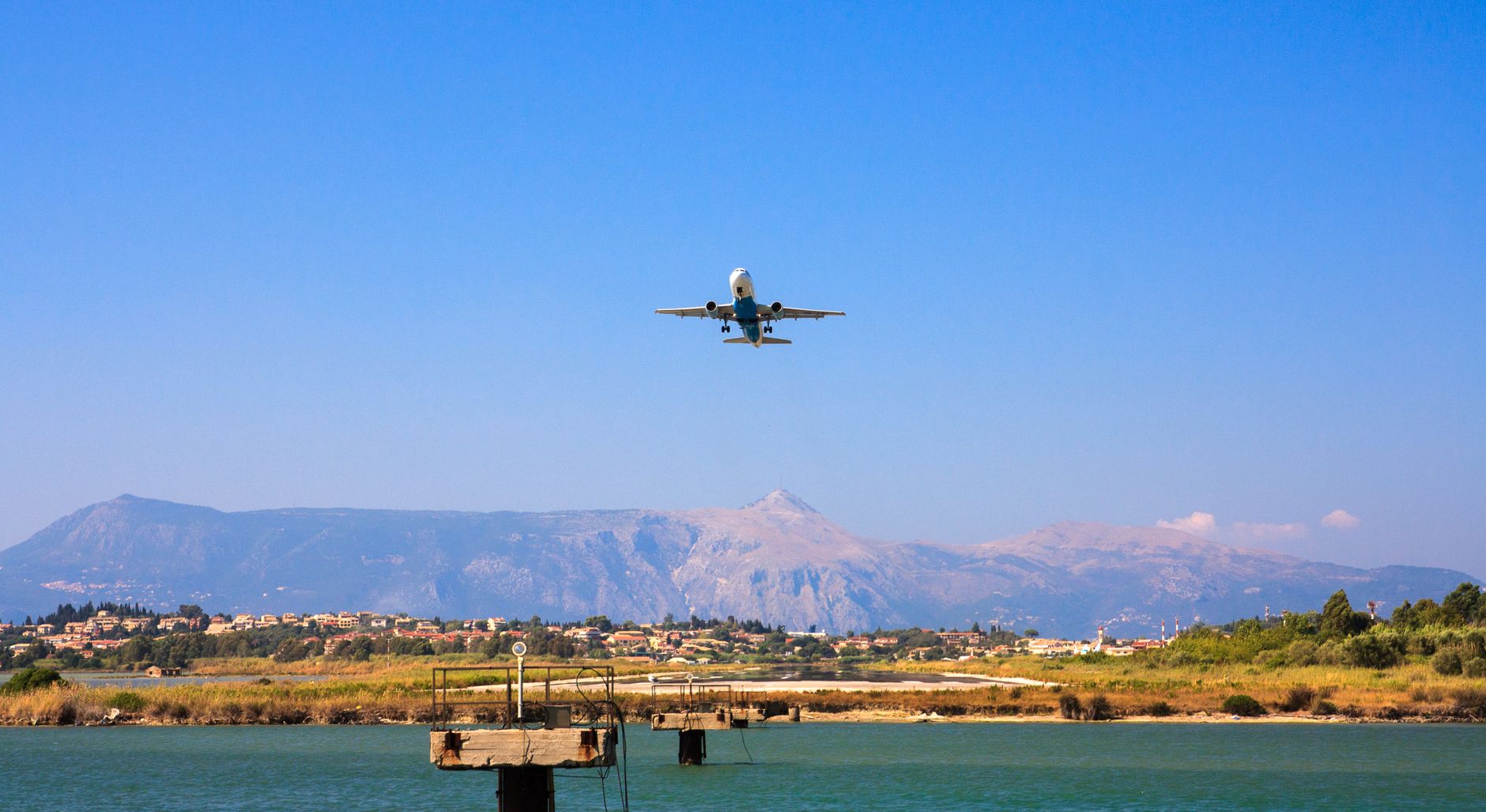 A plane flying over Corfu, Greece with mountains and water below, capturing a vibrant day scene.