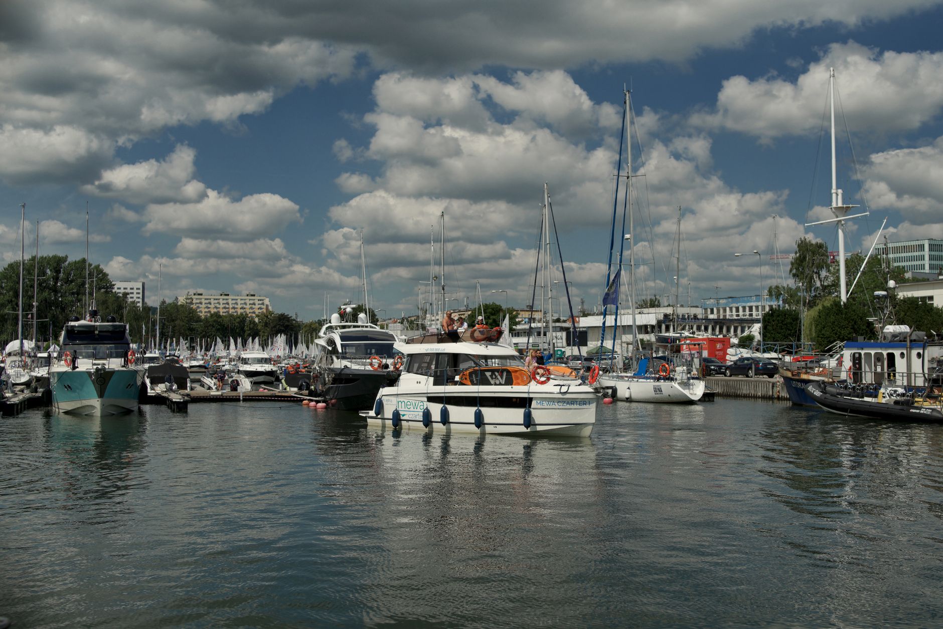 A scenic view of sailboats and yachts at the marina harbor in Gdynia, Poland under a cloudy summer sky.