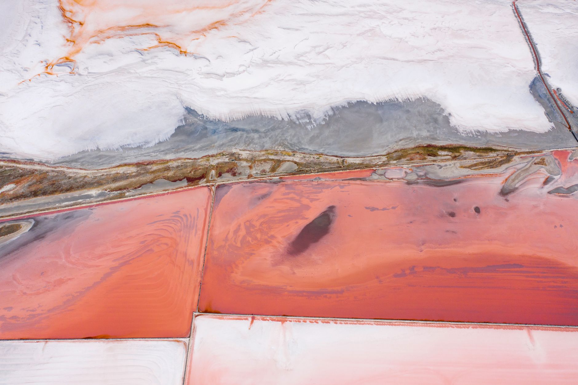 A colorful aerial view of salt flats with striking pink and white patterns.
