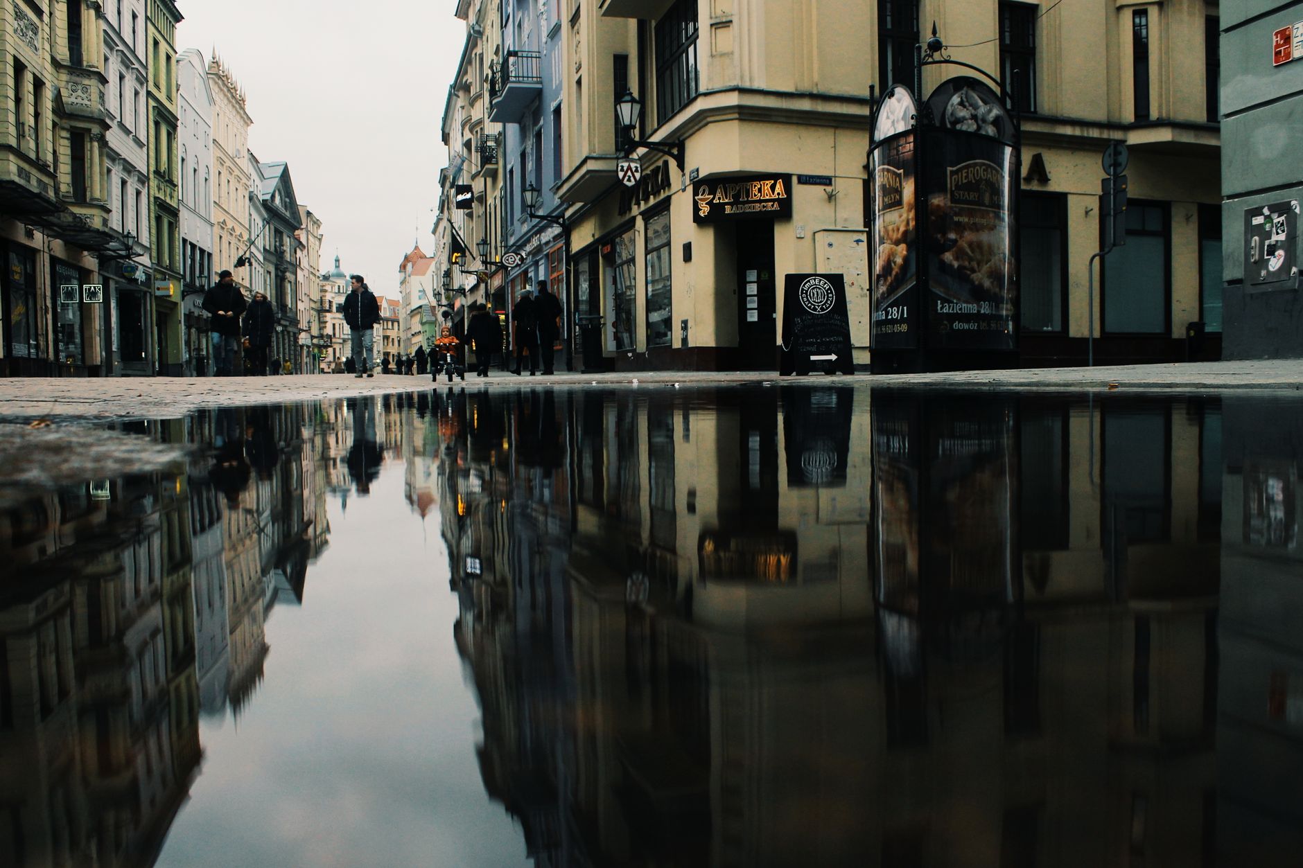 Puddle reflection of historic buildings on a street in Toruń, Poland, creating a serene urban scene.