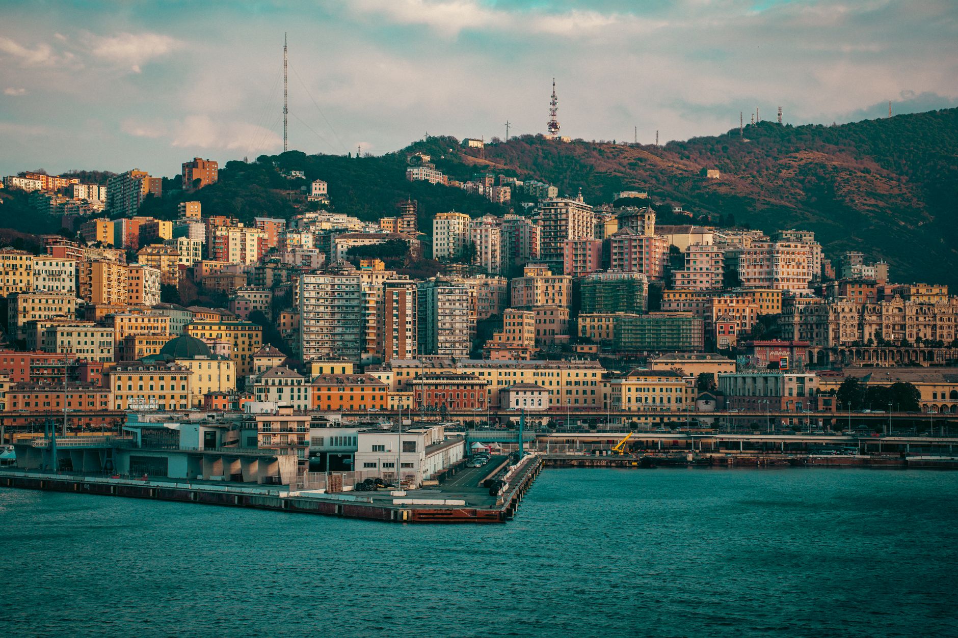 Scenic shot of Genoa's vibrant coastal skyline with colorful buildings against a hilly backdrop.