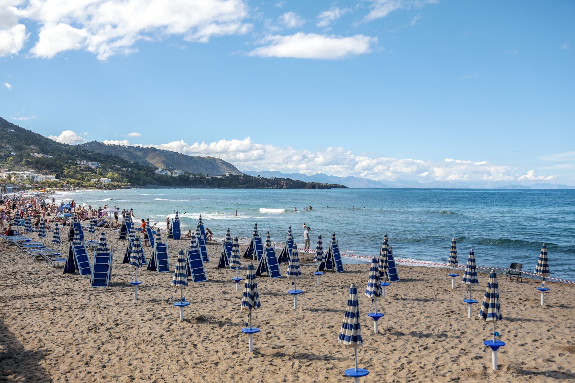 A scenic beach in Sicily, Italy, with rows of umbrellas and people enjoying the sun and sea.
