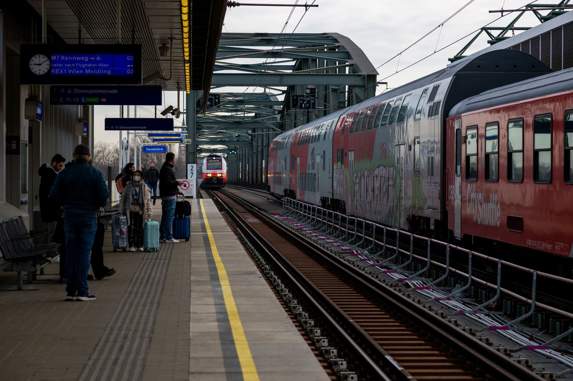 People wait on a European train station platform with approaching trains, showcasing modern travel.
