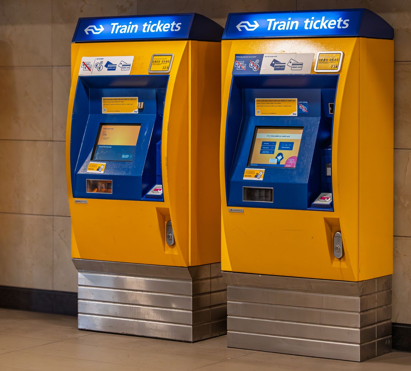 Two vibrant yellow and blue train ticket machines in an indoor station setting.