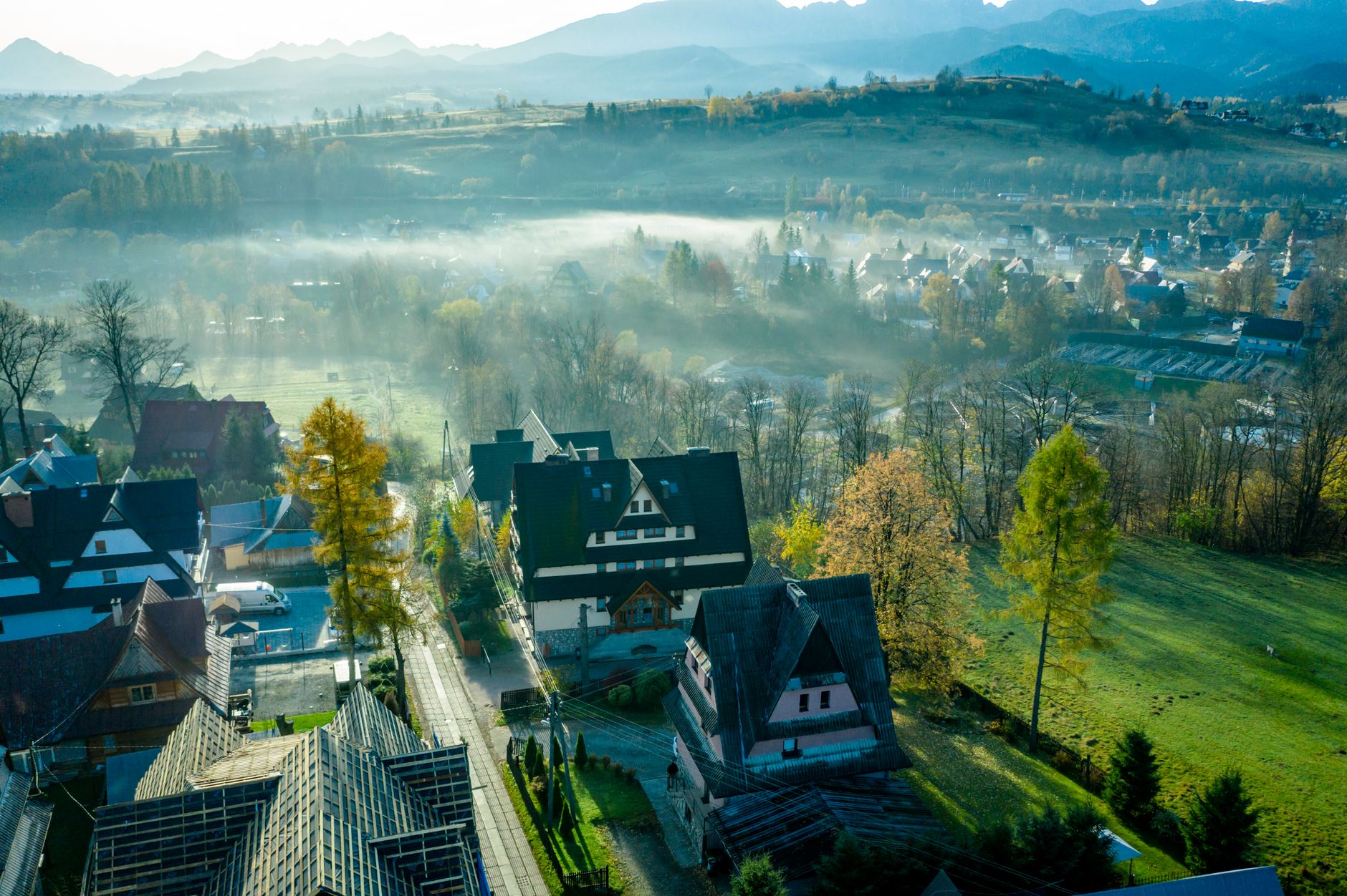 Aerial view of Zakopane with fog covering the landscape, traditional houses, and vibrant autumn colors.