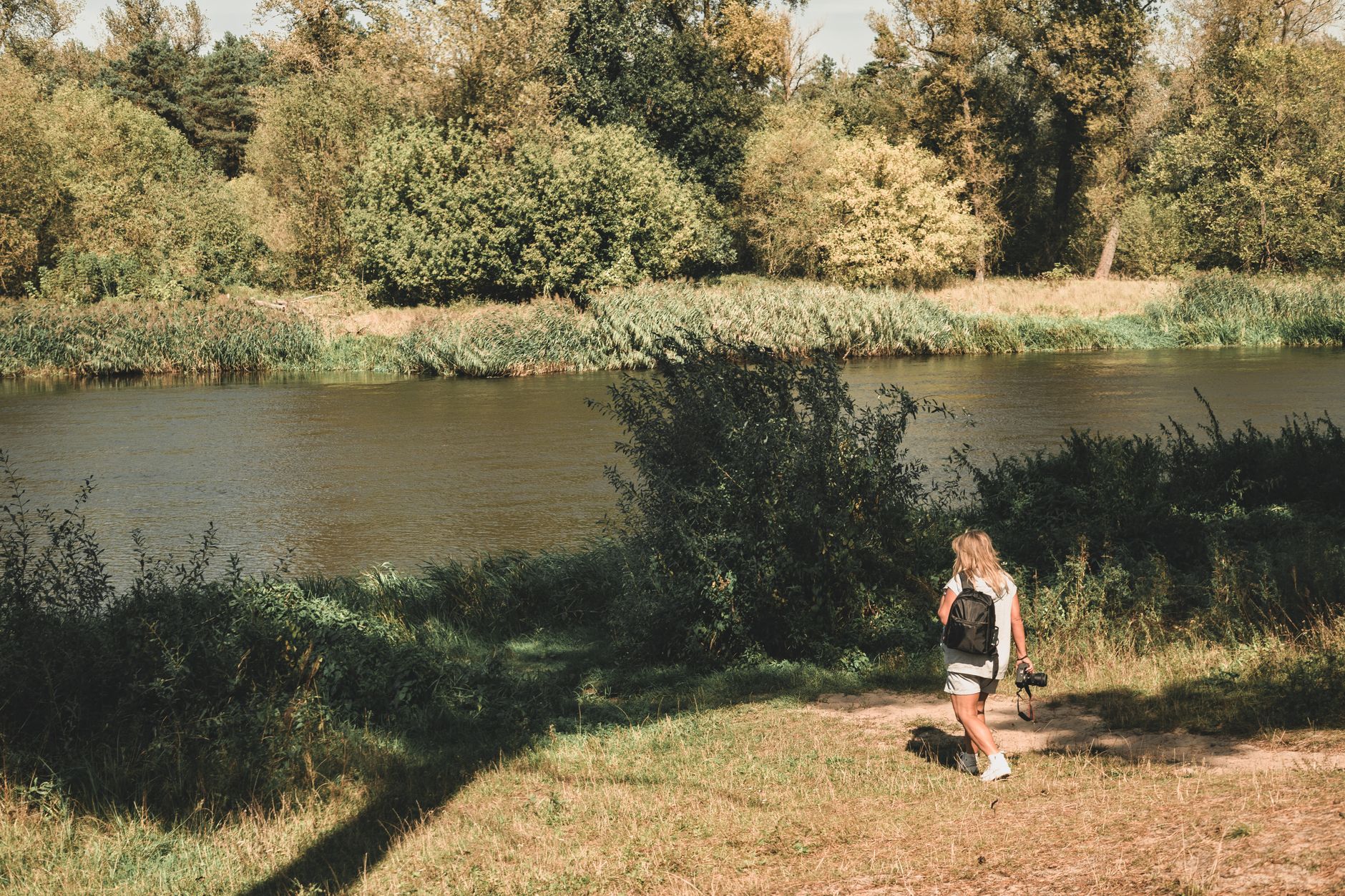 A woman photographer walks by a river in lush greenery in Poland.