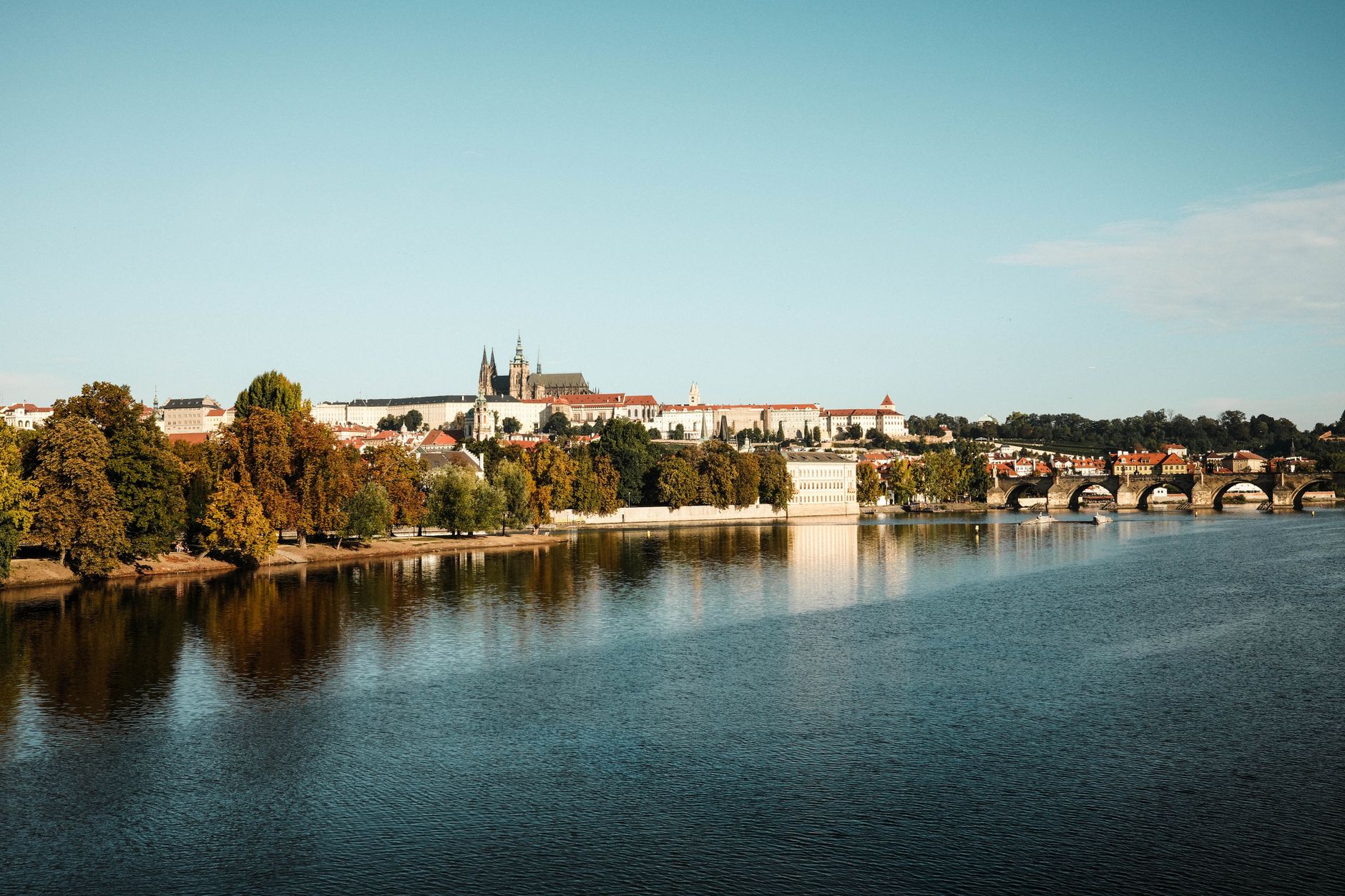 Scenic view of Prague Castle and Charles Bridge reflecting on the Vltava River in autumn light.