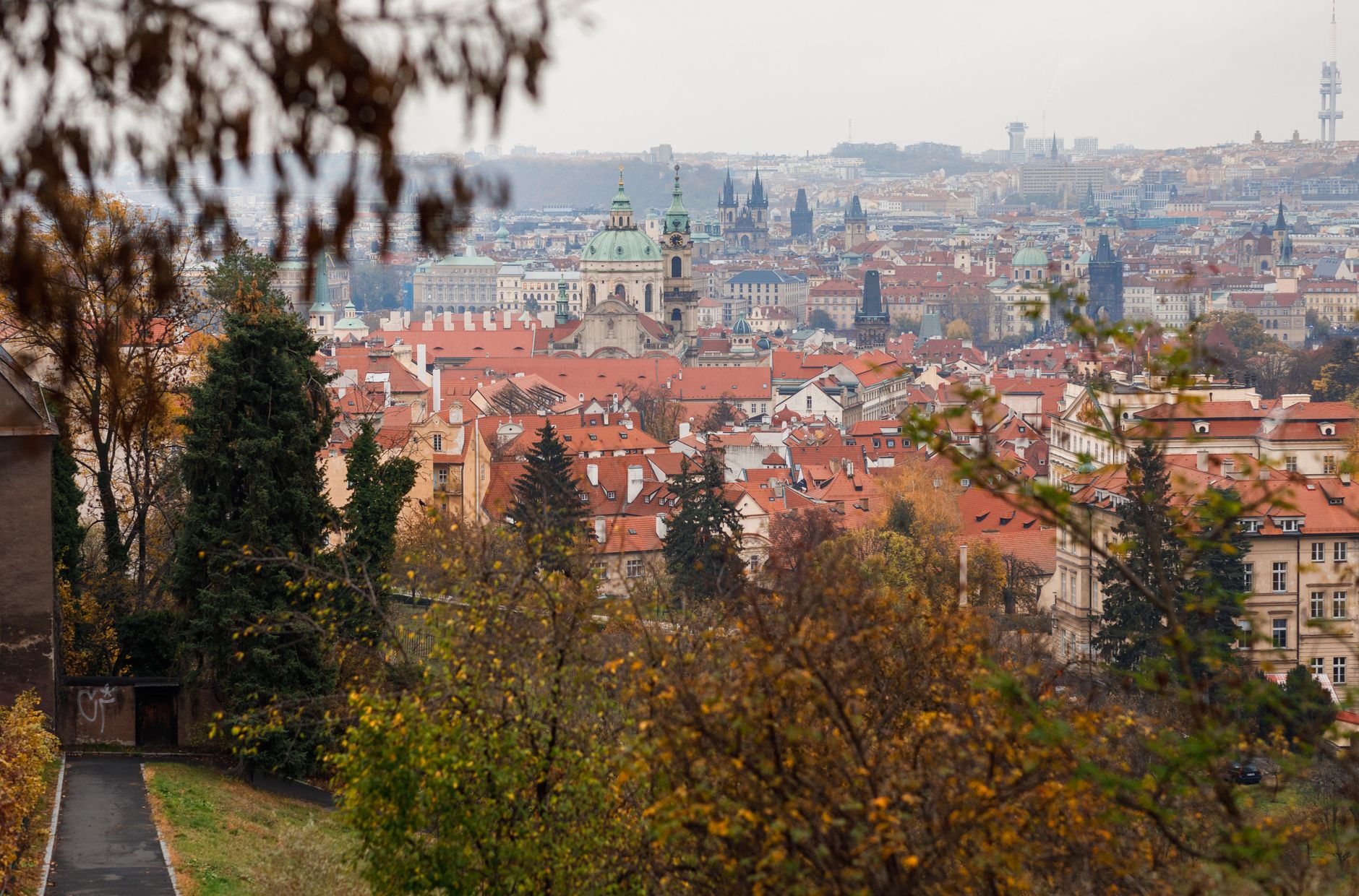 Captivating cityscape of Prague showcasing historic red roofs, churches, and vibrant autumn foliage.