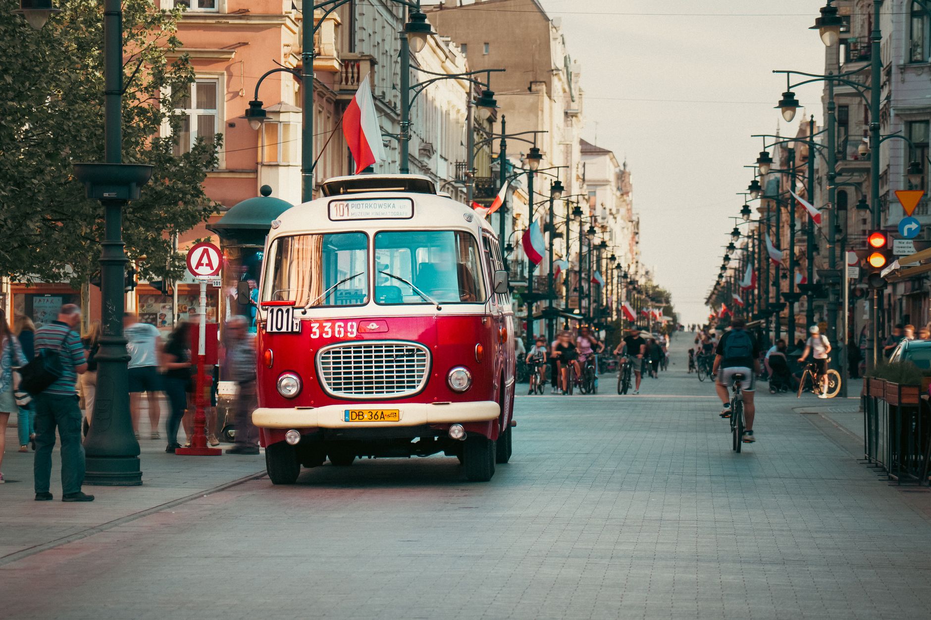 Historic red bus in motion on Piotrkowska Street, Łódź, Poland, showcasing urban city life.