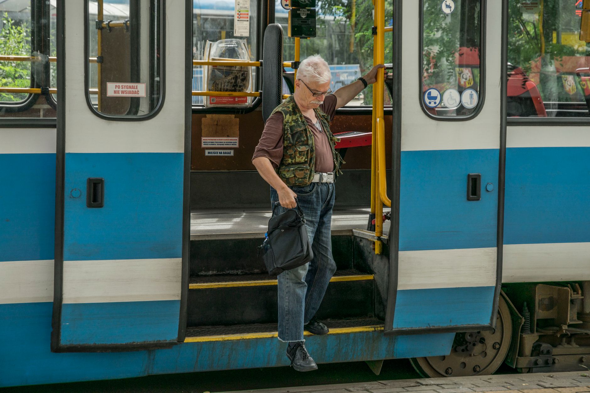 A senior adult stepping off a tram in Wrocław, illustrating urban transit life.