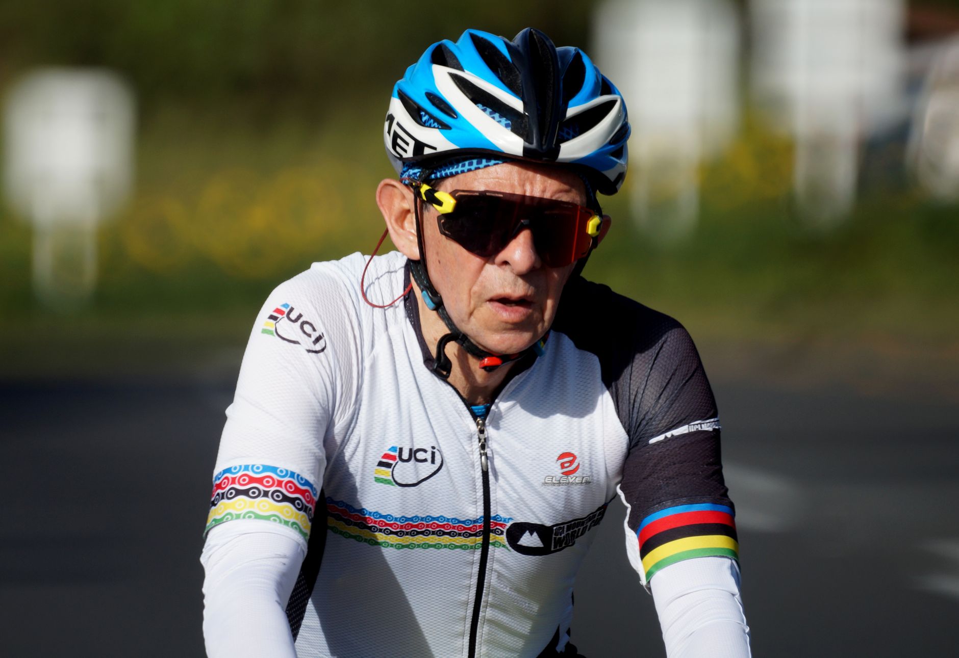 Elderly cyclist wearing helmet and sportswear, riding outdoors in daylight.