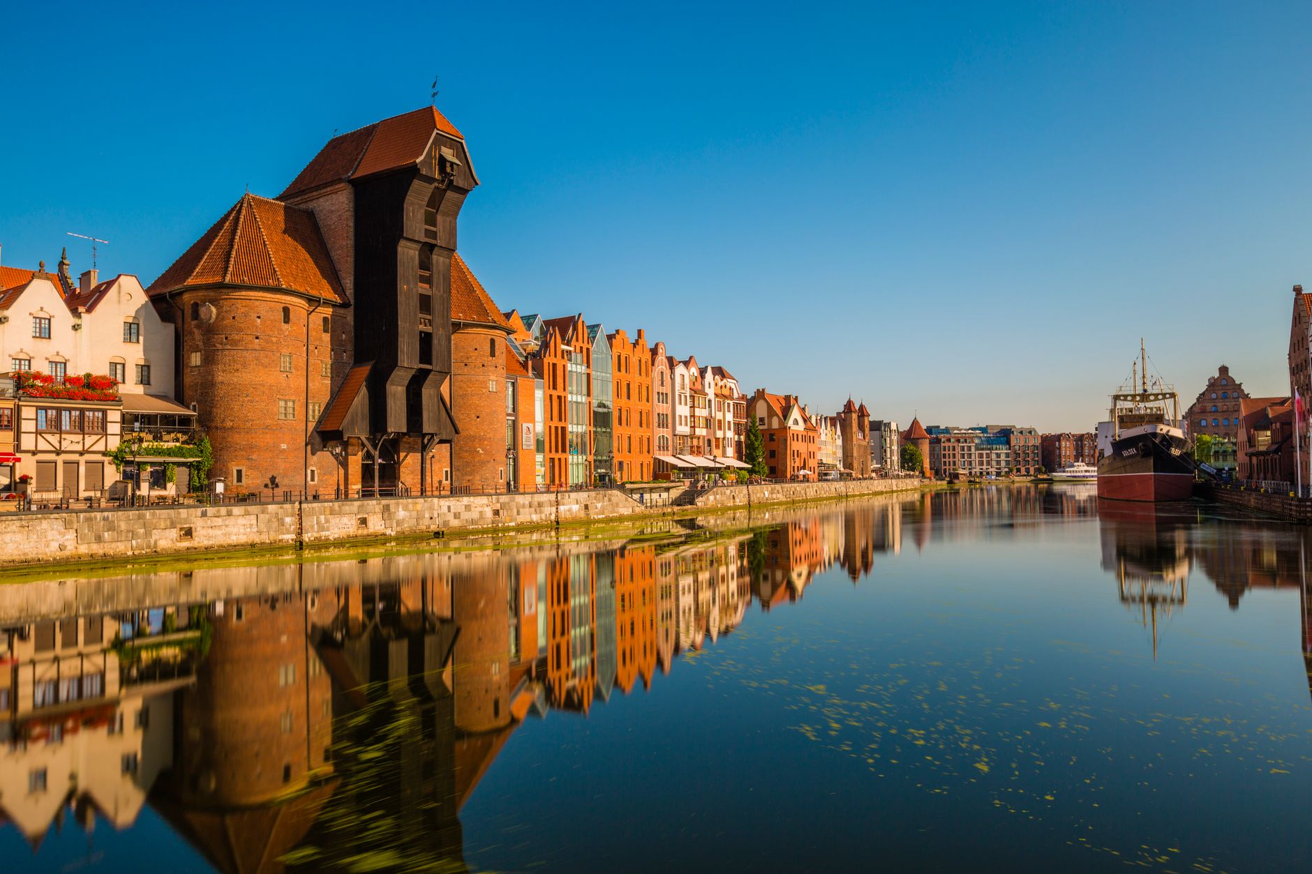 Beautiful view of the historic crane and waterfront buildings reflecting in the calm waters of Gdańsk, Poland.