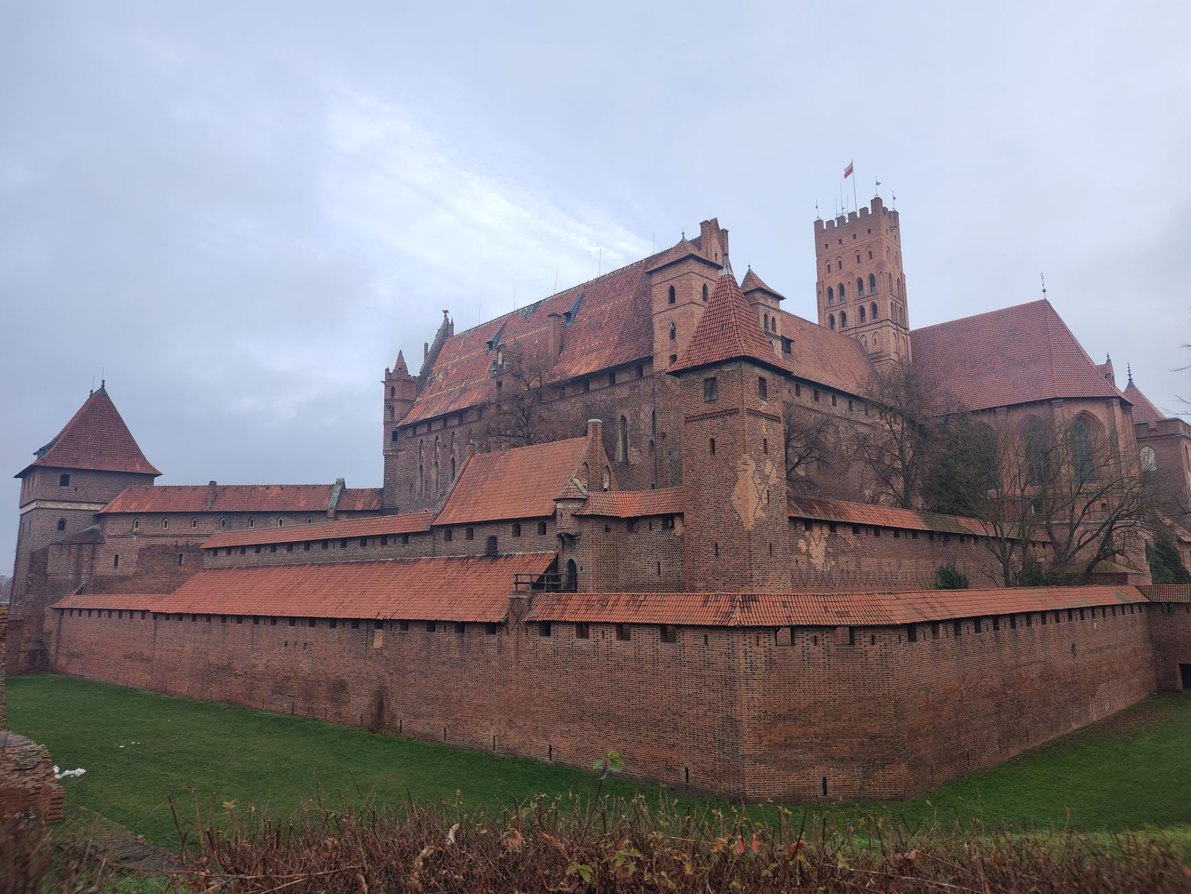 Stunning view of the historic Malbork Castle in Poland, with red brick architecture against a cloudy sky.