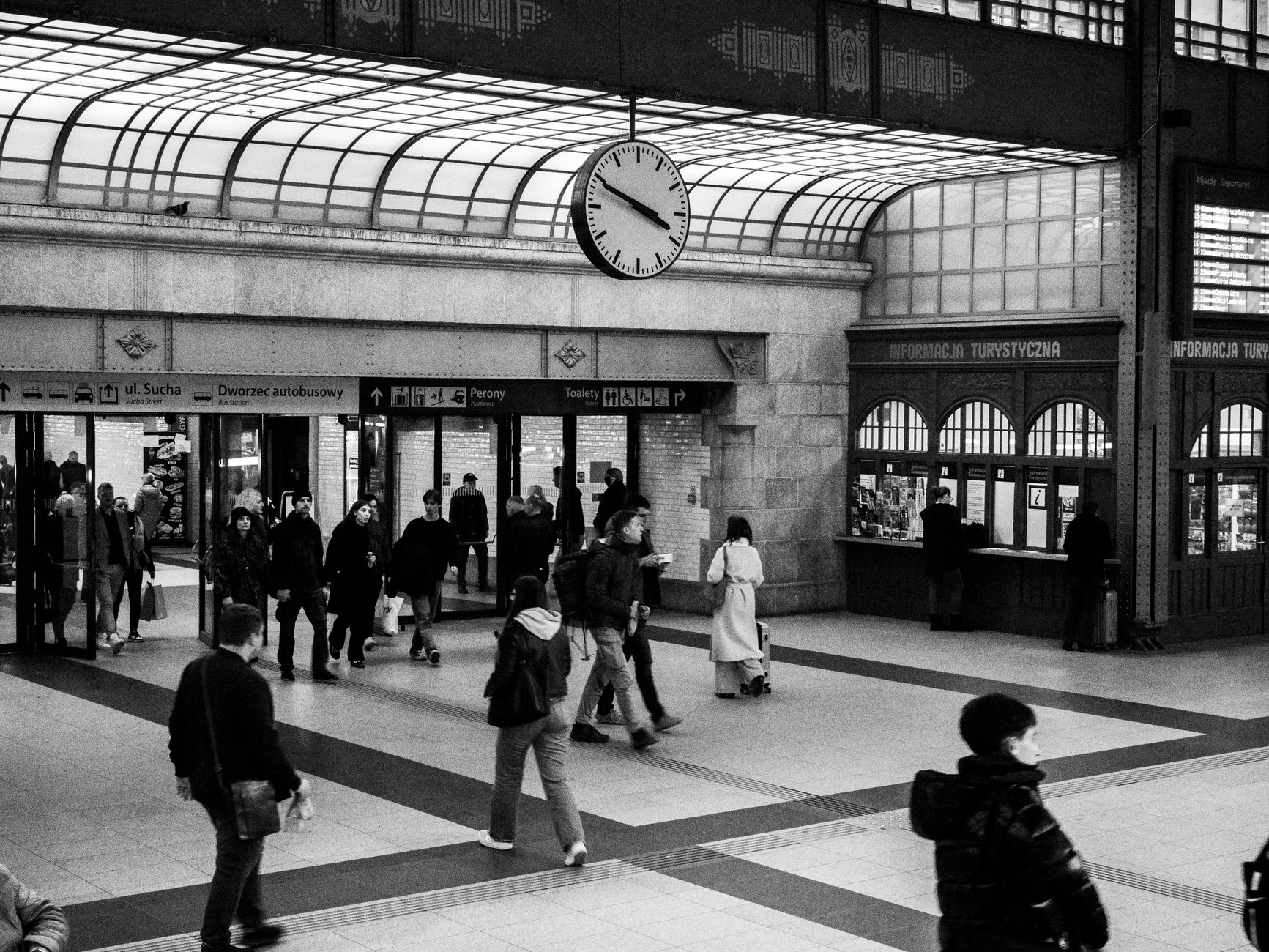 Monochrome view of a crowded train station with a prominent clock and ticket counters.
