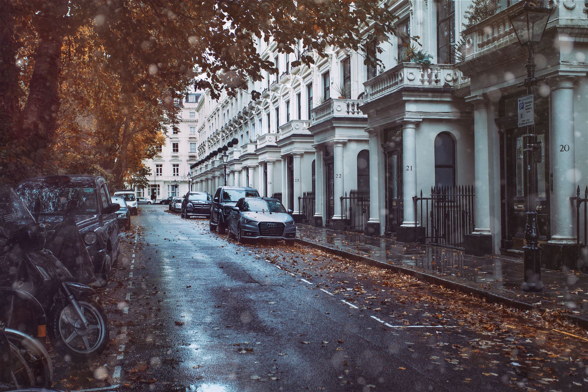 A picturesque London street with parked cars and classic architecture on a rainy autumn day.